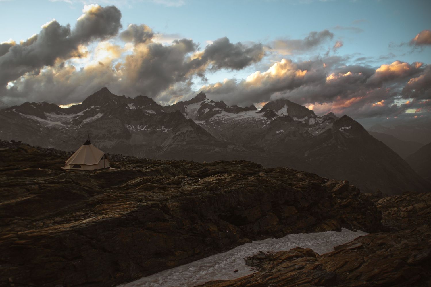 Dramatic mountain landscape at sunset with stormy clouds and snow-capped peaks.