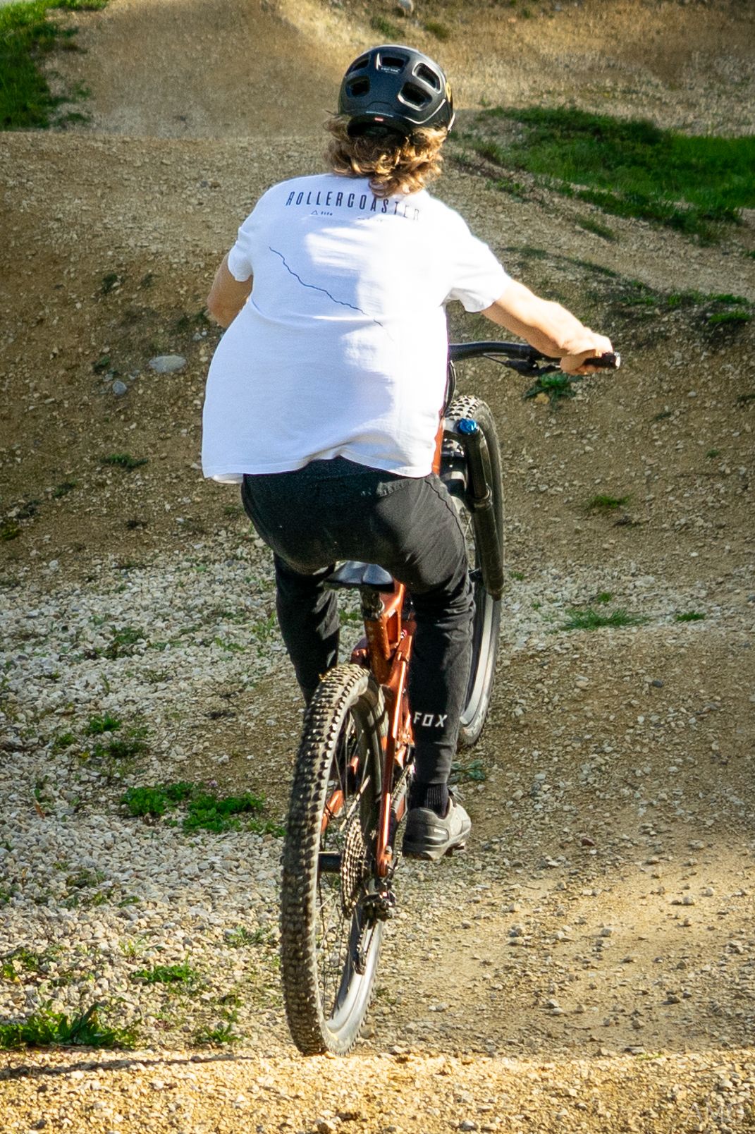 Mountain biker riding dirt trail wearing white t-shirt and helmet.