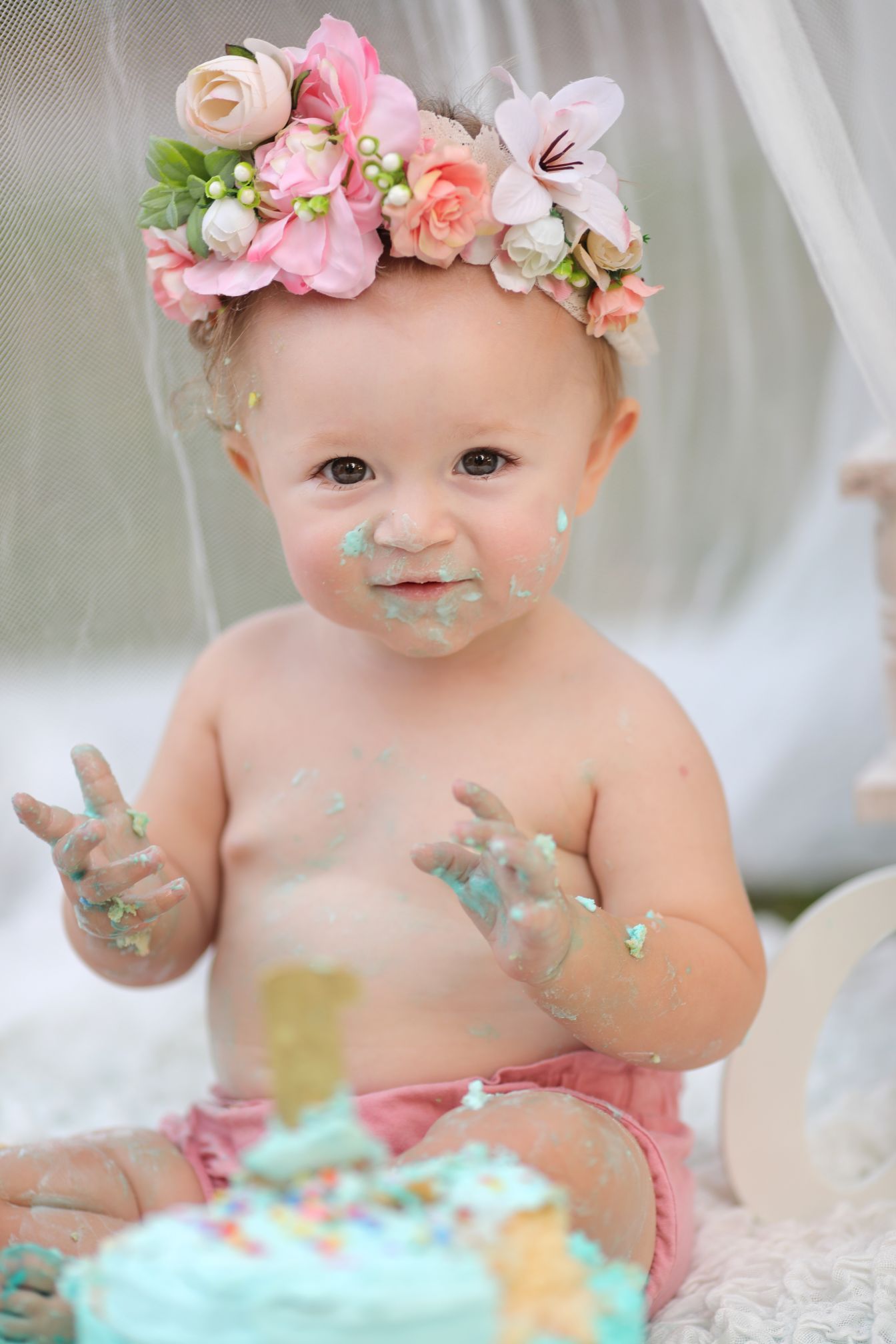 Baby wearing floral crown with turquoise frosting on face during cake smash photo session.