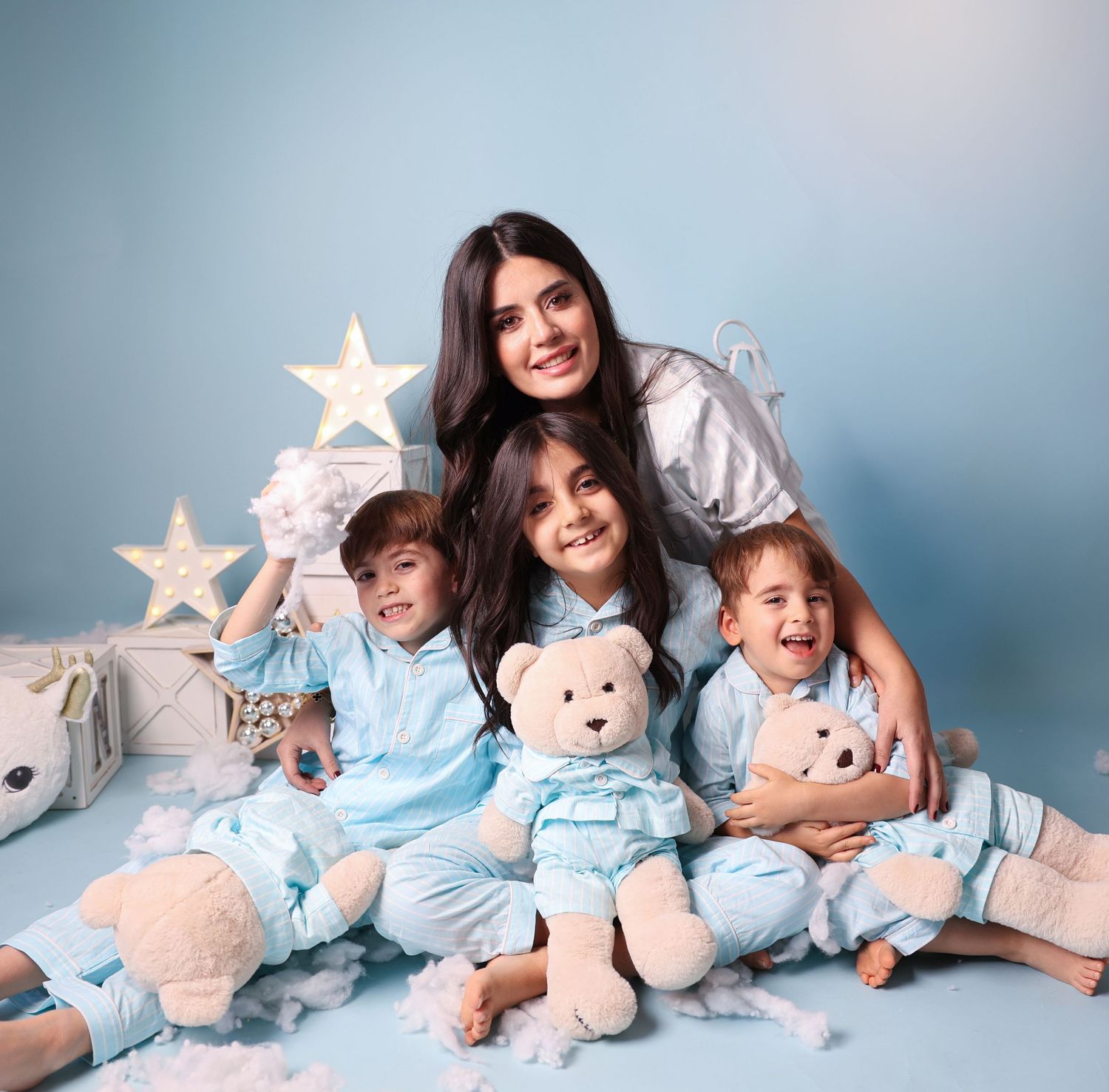 Cozy family portrait with teddy bears and star decorations against blue backdrop.