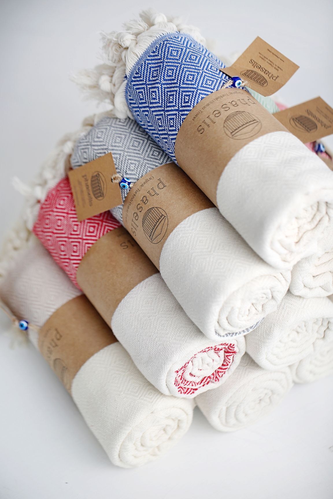 Collection of rolled Turkish towels in white, blue and pink patterns with kraft paper bands.