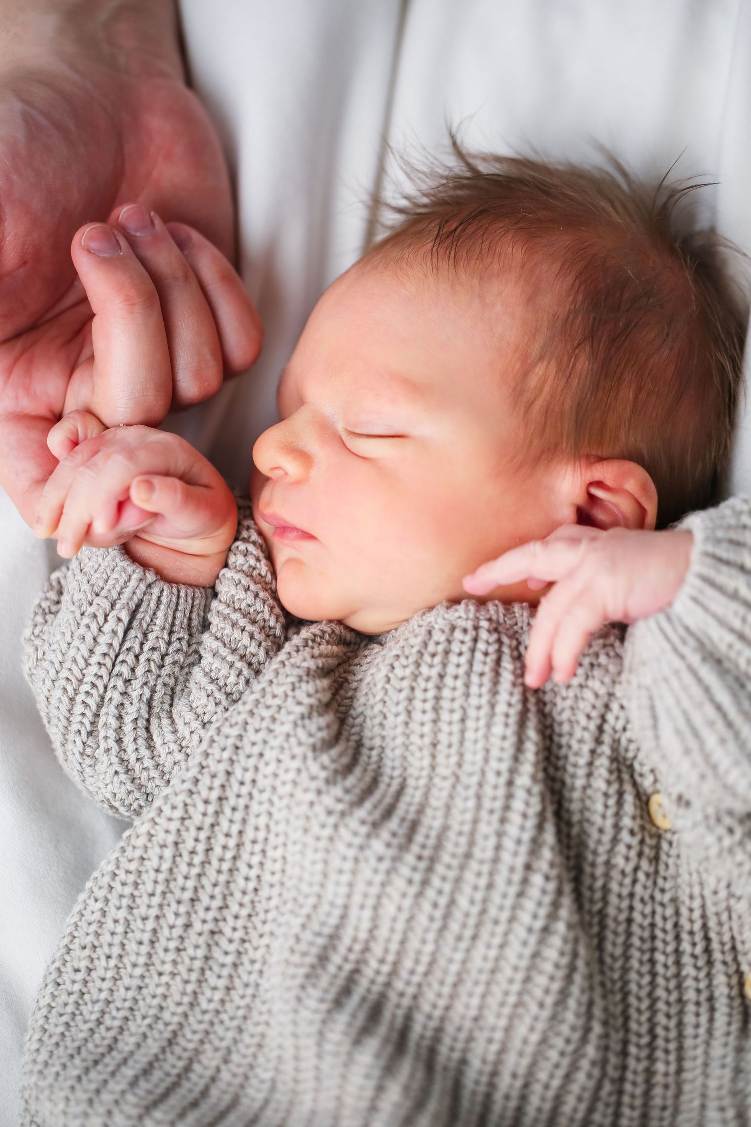 Peaceful sleeping newborn wearing cozy knit sweater on white bedding.