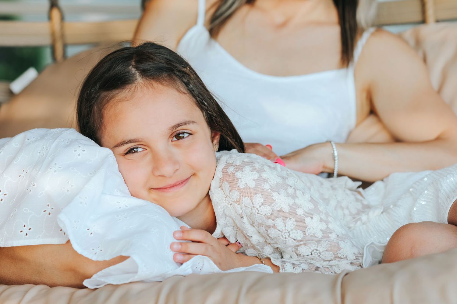 Portrait of a person lying on white bedding with a gentle smile.