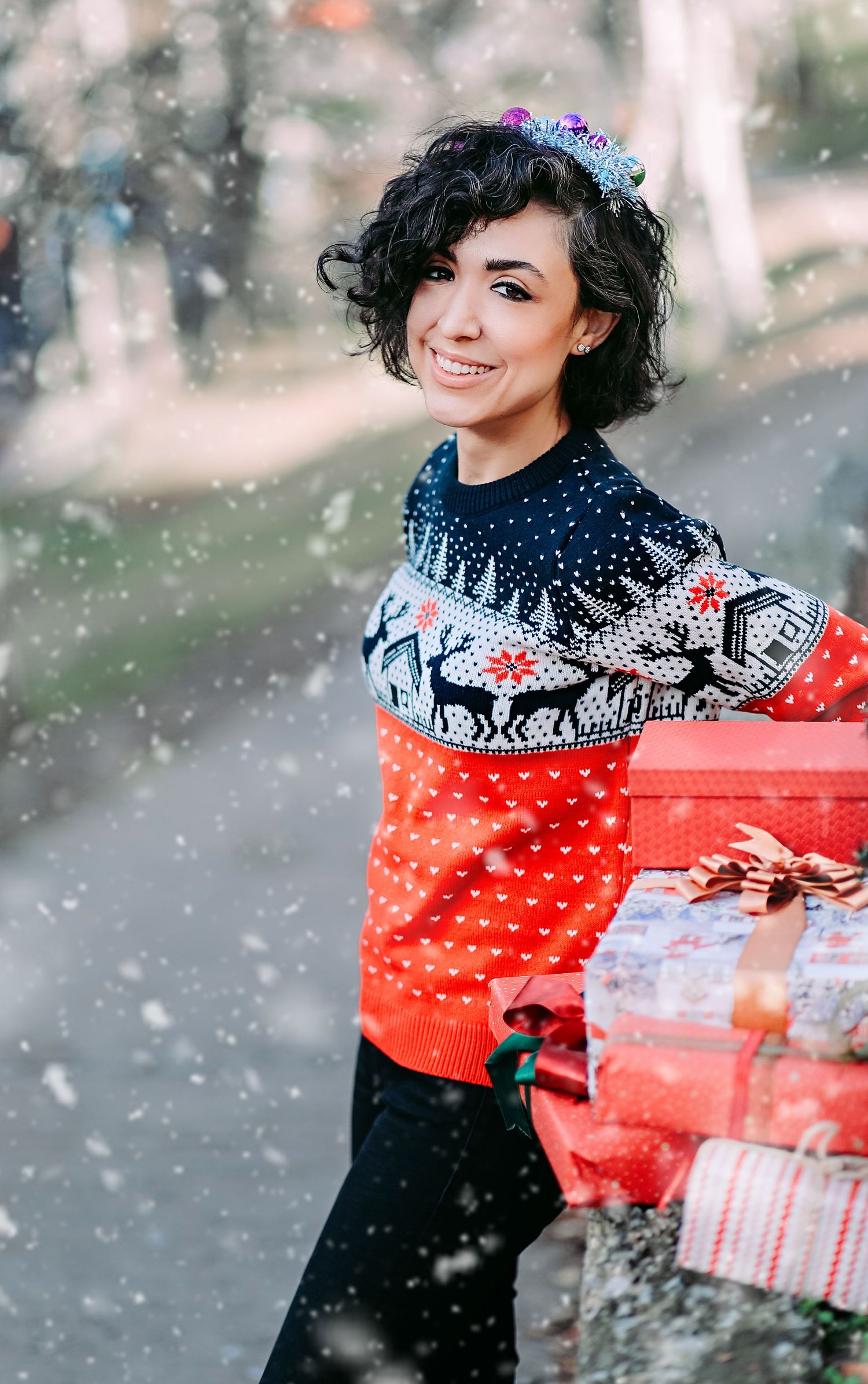 Person in festive holiday sweater carrying wrapped presents while snow falls.