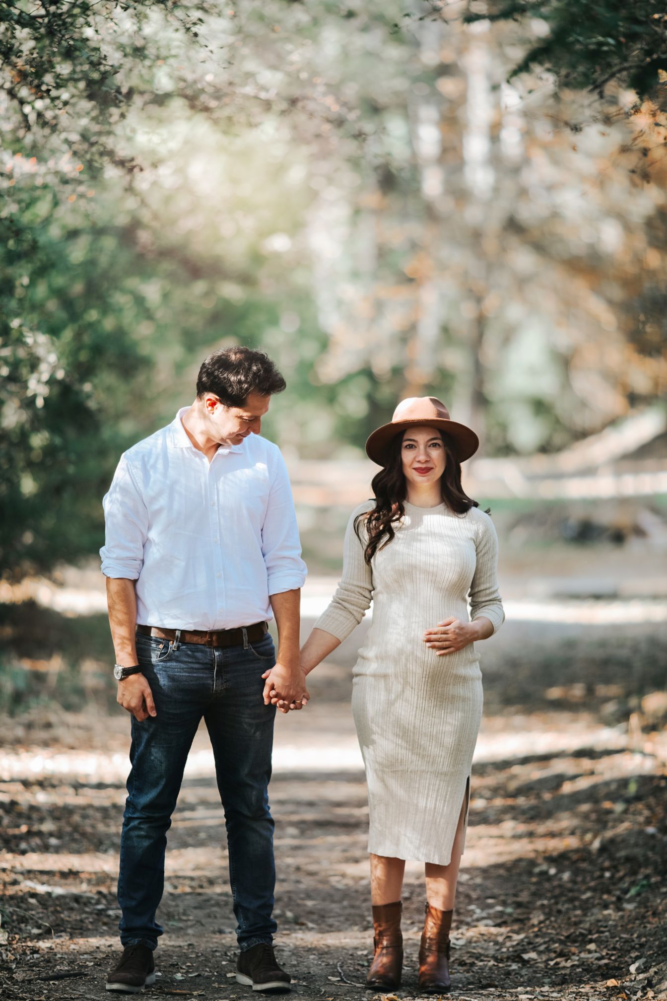 Romantic couple holding hands while walking on forest path in autumn.