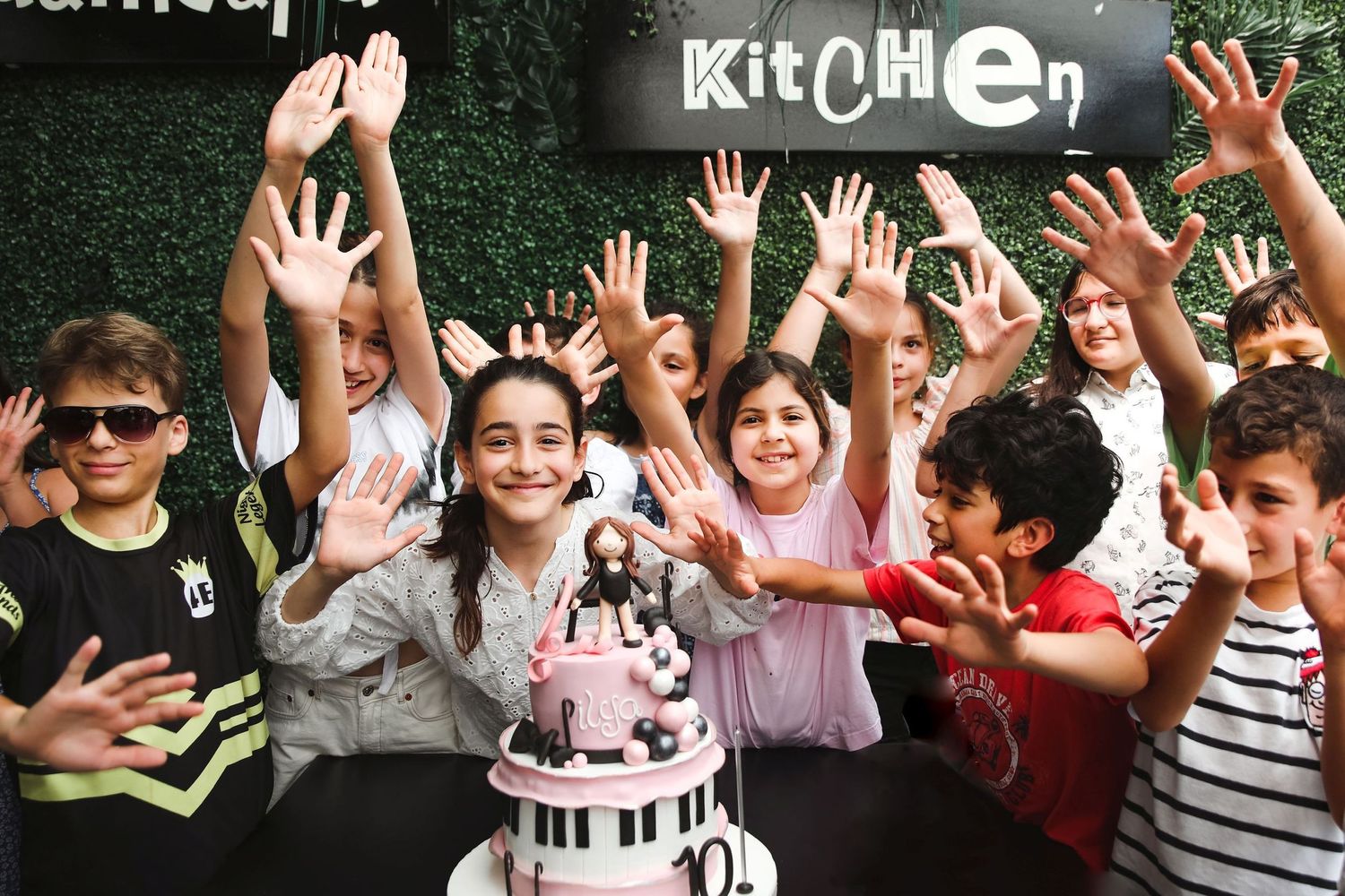 Kids celebrating at a party with raised hands around a piano-themed birthday cake.