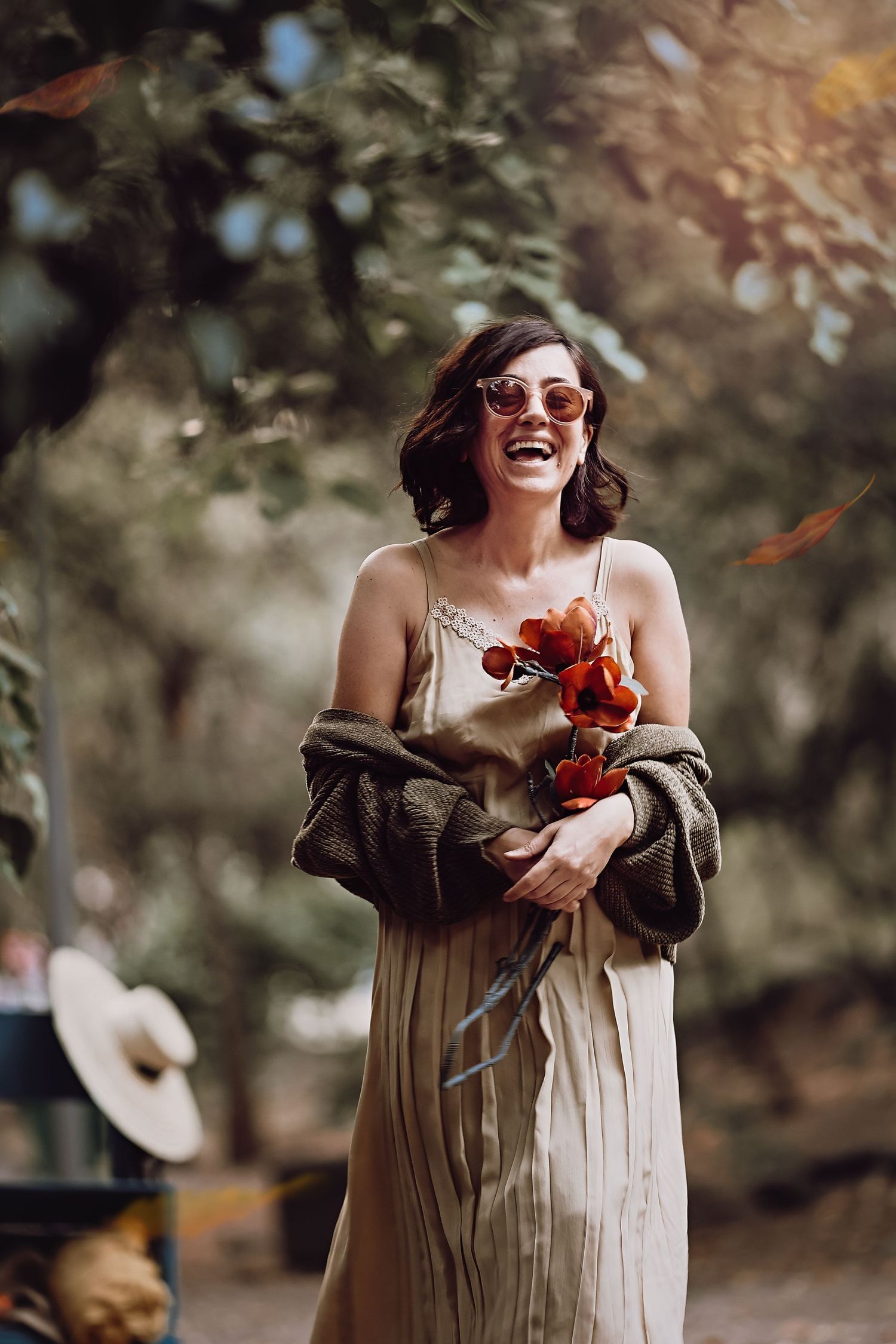 A joyful portrait of someone in a casual dress holding red flowers in a natural outdoor setting.