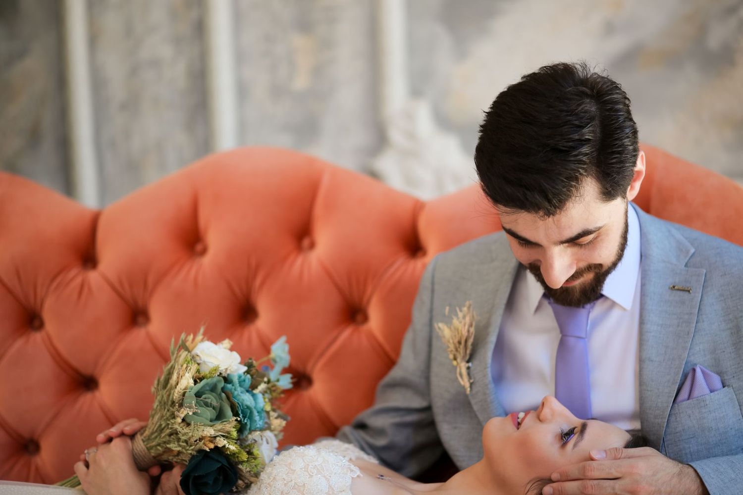 An intimate couple moment captured on a tufted orange sofa with floral decor.