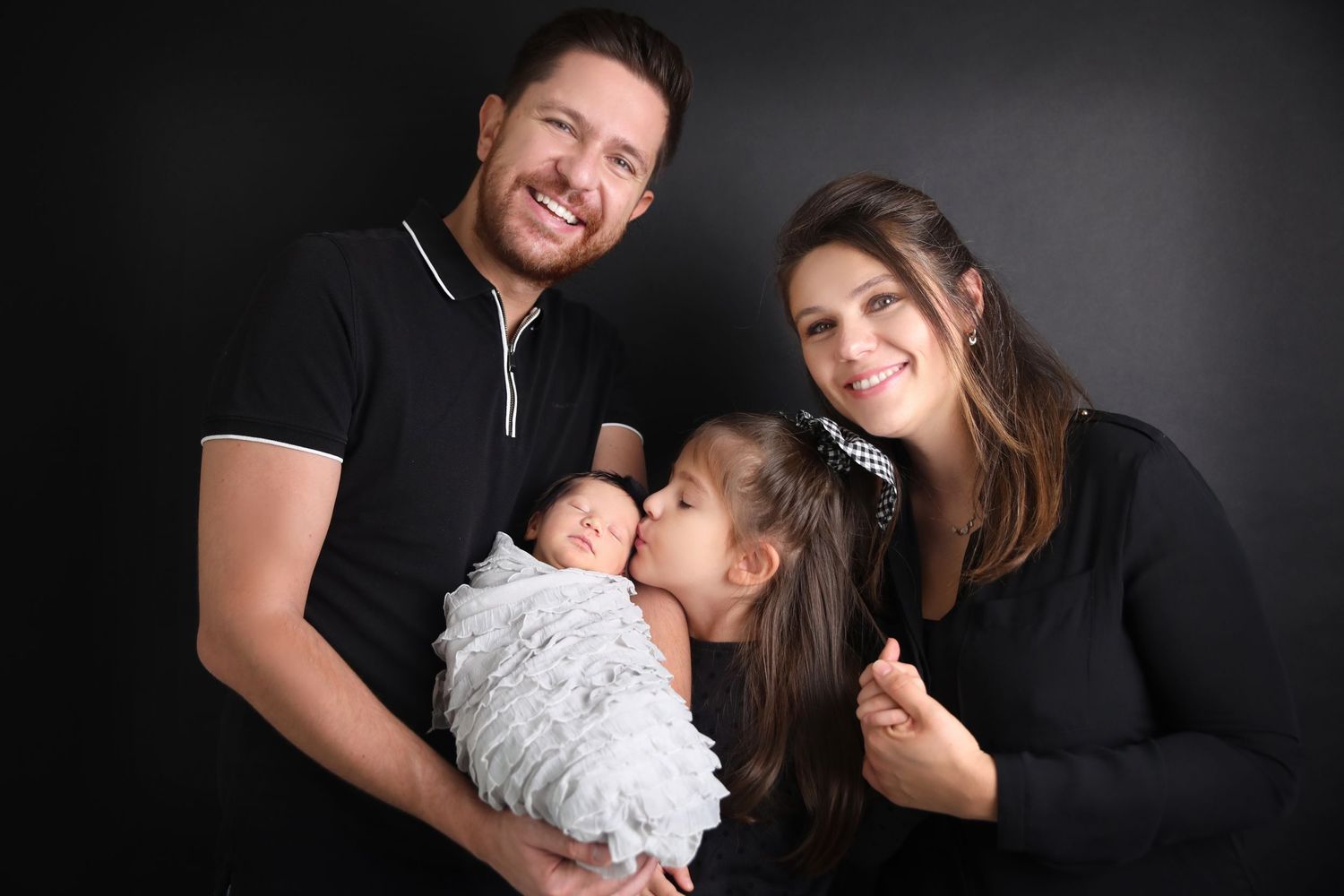 Studio portrait of family in black outfits against dark background.