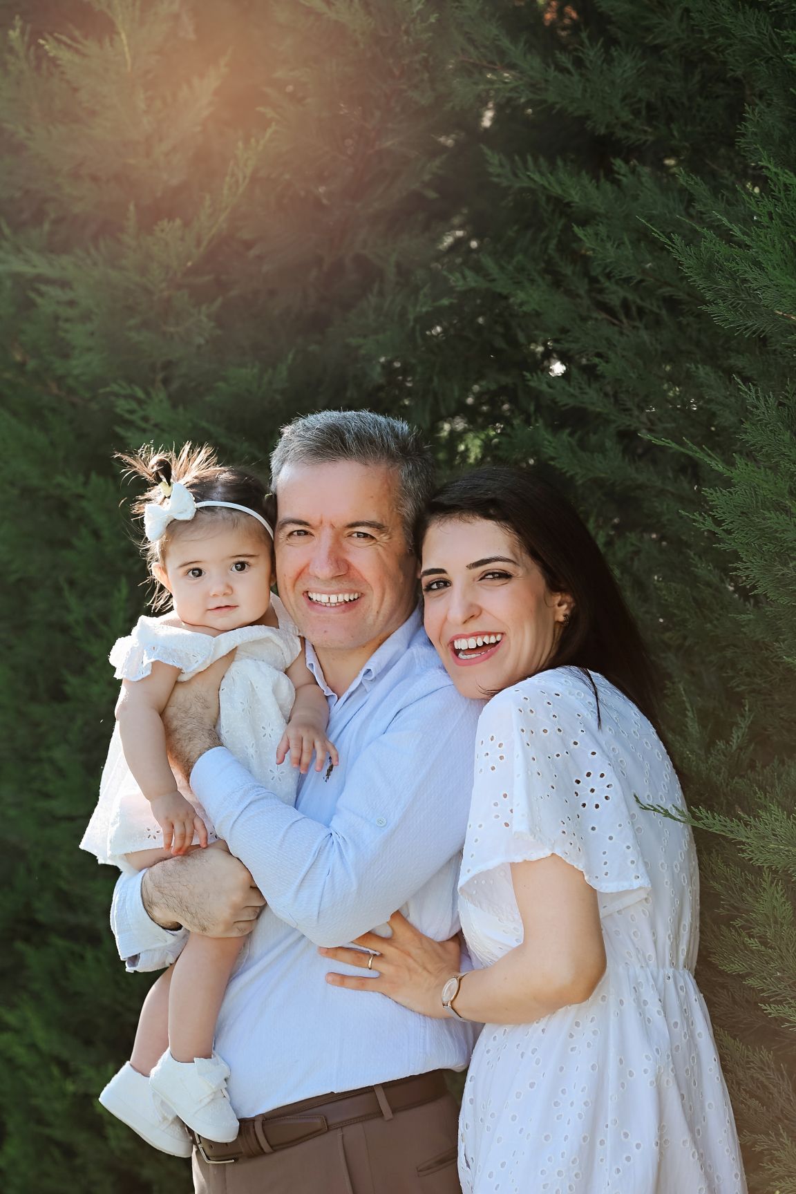 A joyful family portrait taken outdoors against evergreen trees.