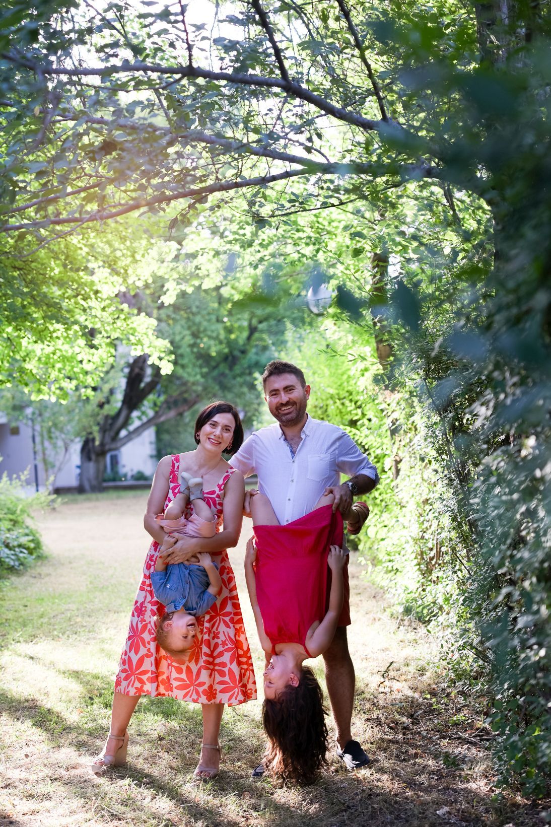 Couple in summer outfits walking with their dog on a sunlit garden path.