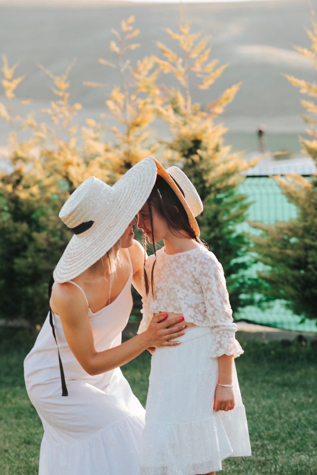 A tender outdoor moment between two people in white dresses and sun hats.