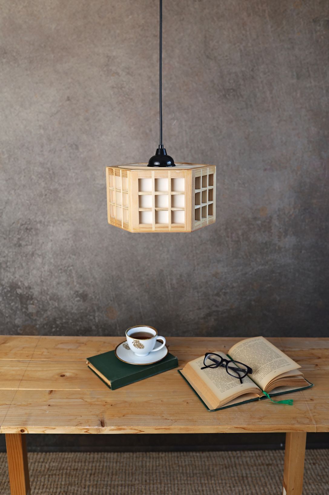 Minimalist wooden pendant lamp over table with coffee, book and reading glasses.