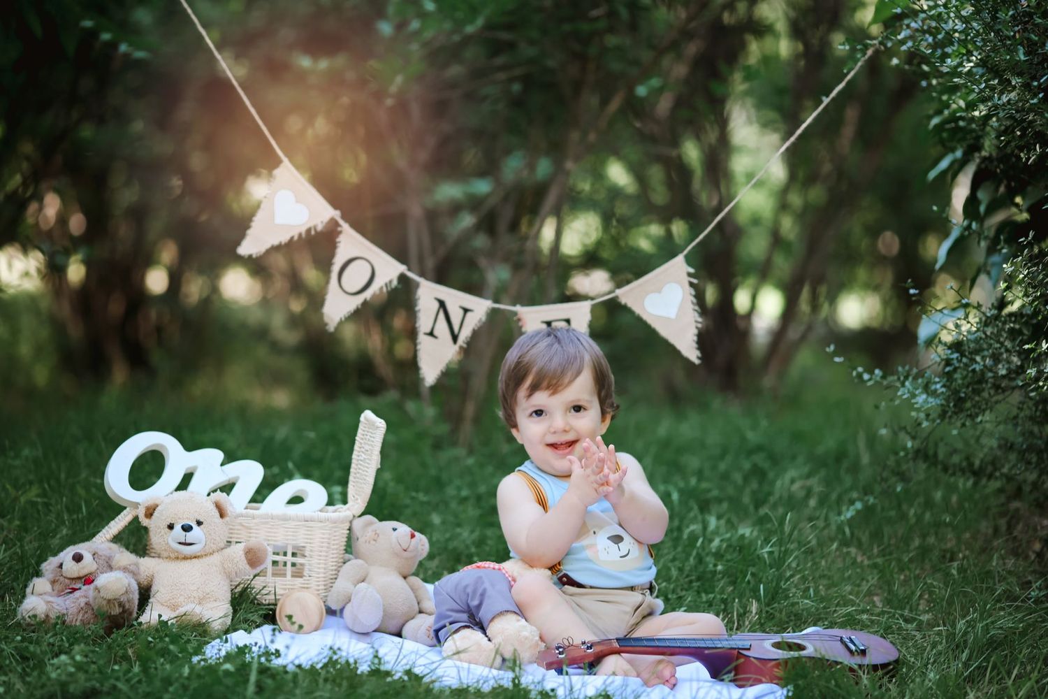 A baby sitting on a blanket with stuffed animals and decorative bunting outdoors.