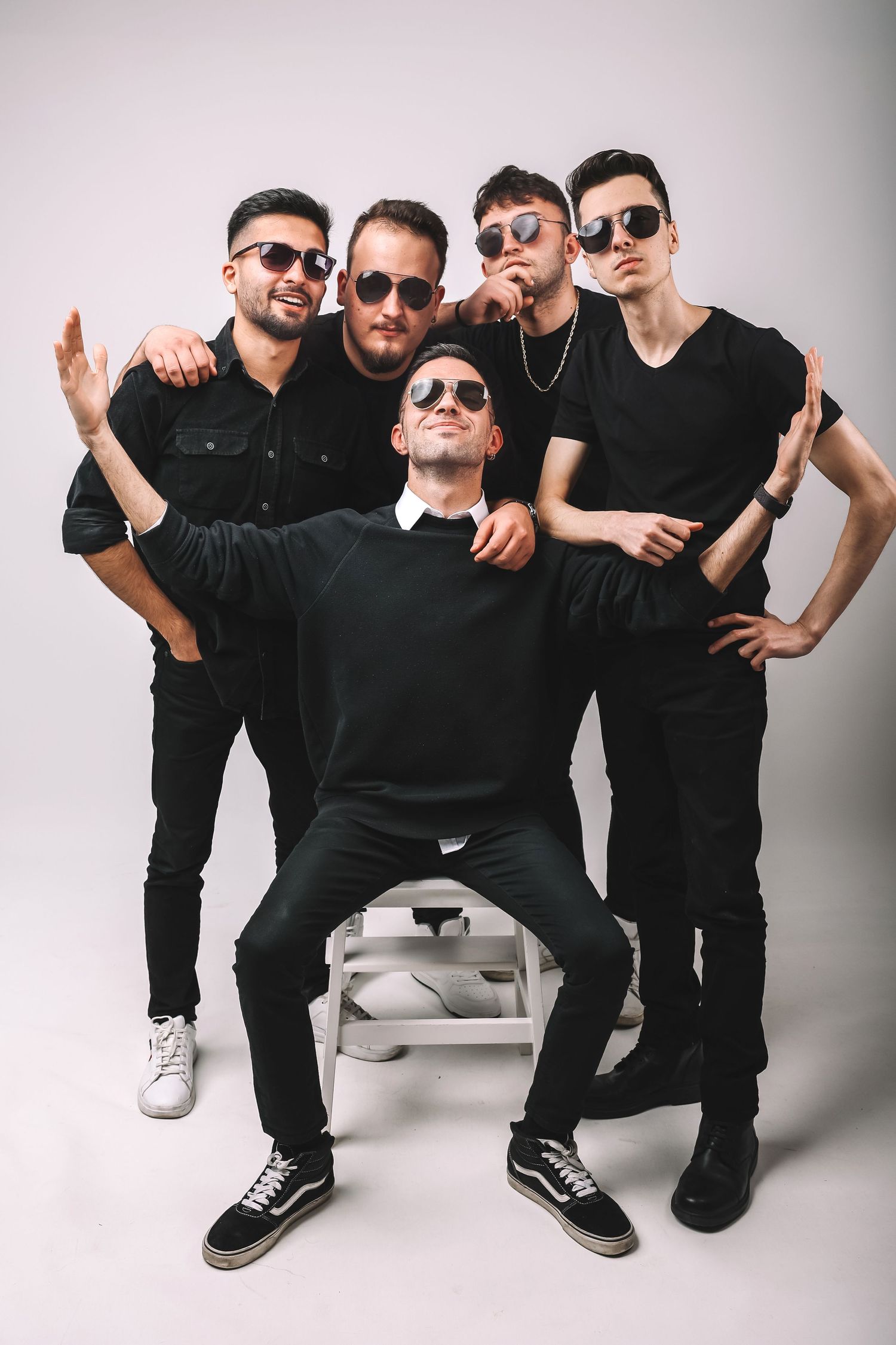 Music band members dressed in all black outfits and sunglasses pose together for a stylish group photo.