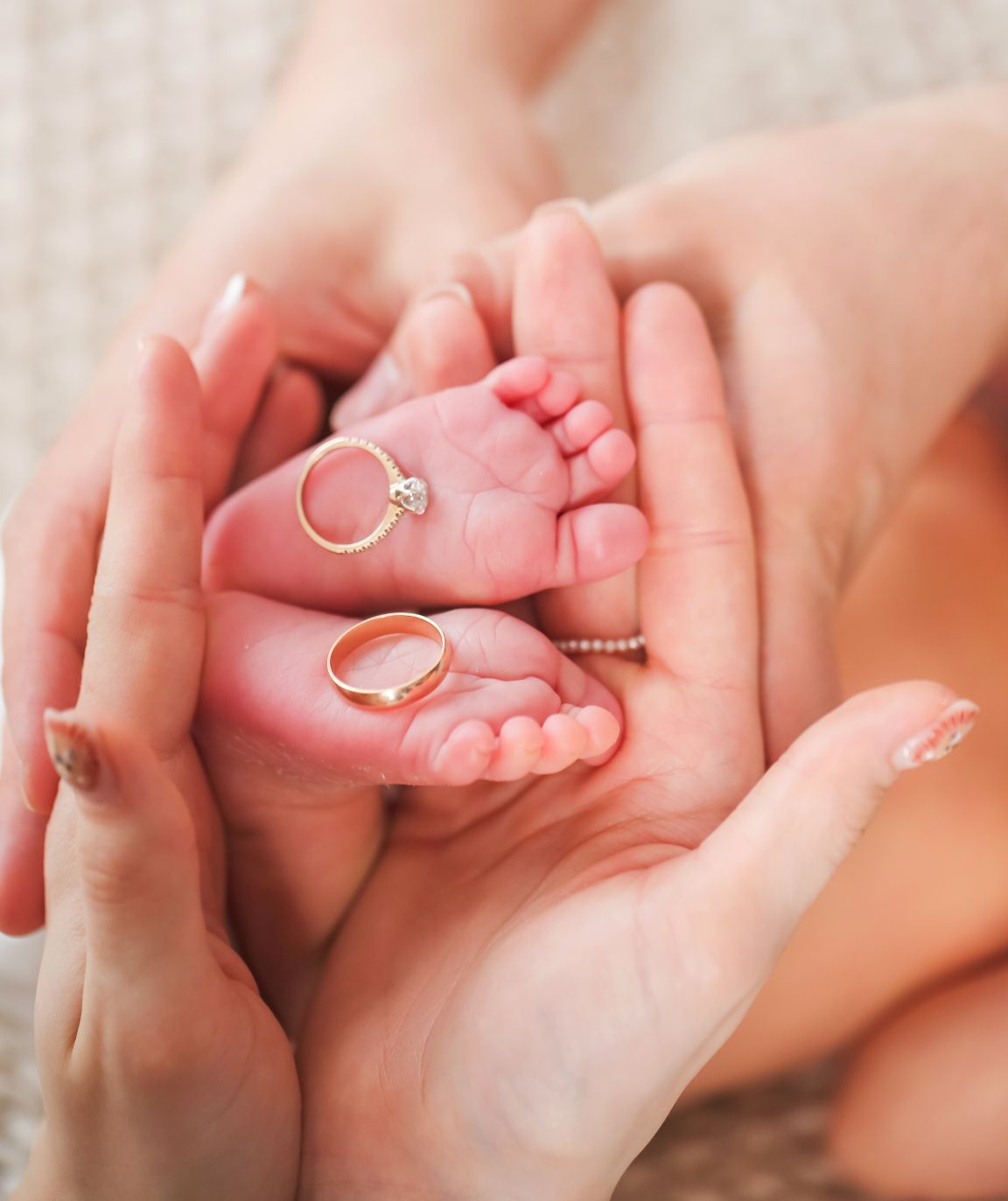 Close-up of tiny baby feet cradled in hands with wedding rings placed on them.