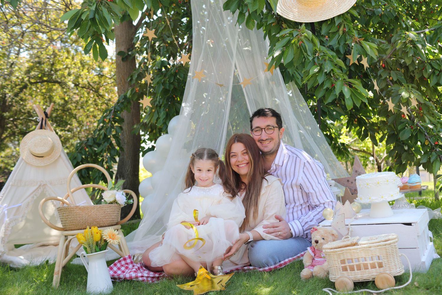 Family picnic setup with white teepee tent and vintage decorations in a garden setting.