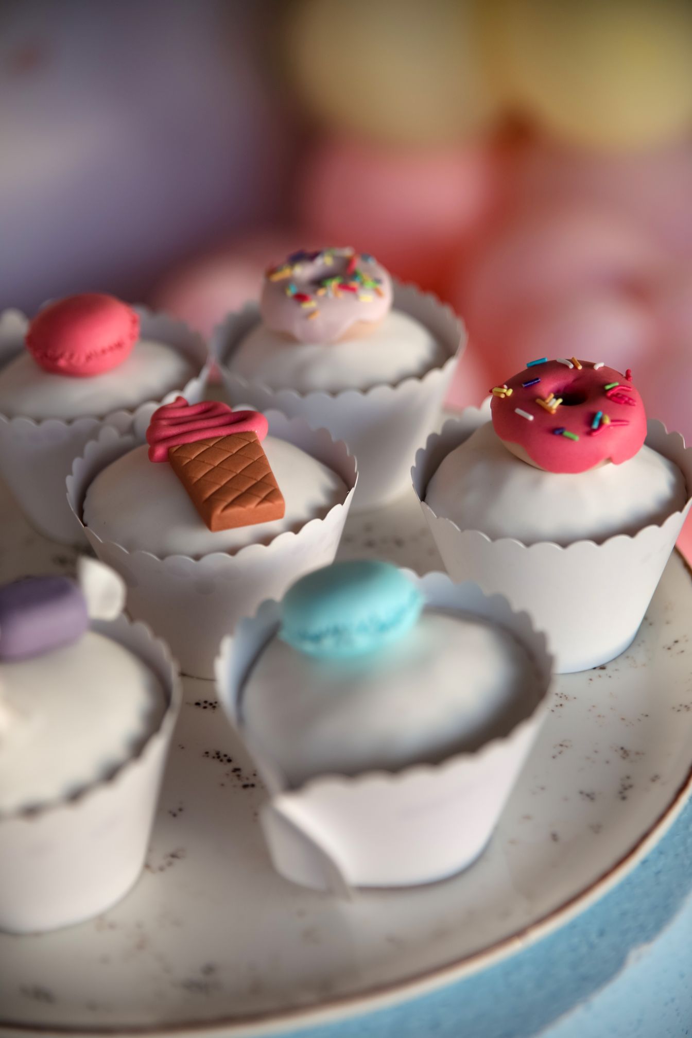 Decorative mini cupcakes topped with macarons and pink frosting on white plate.