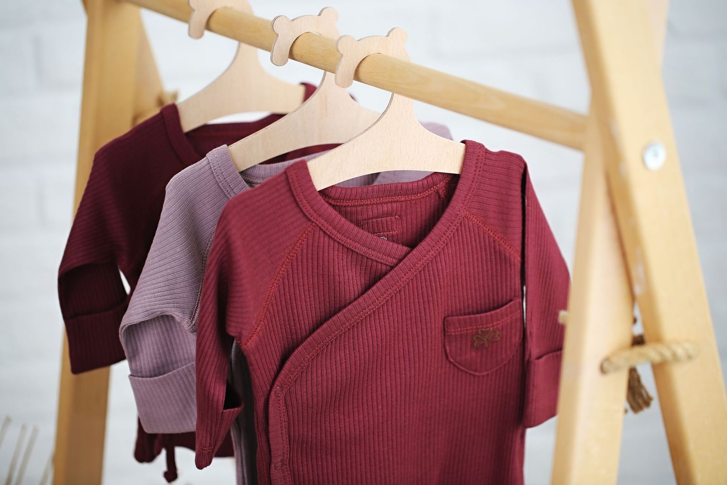 Baby clothes in burgundy and pink tones hanging on wooden rack.