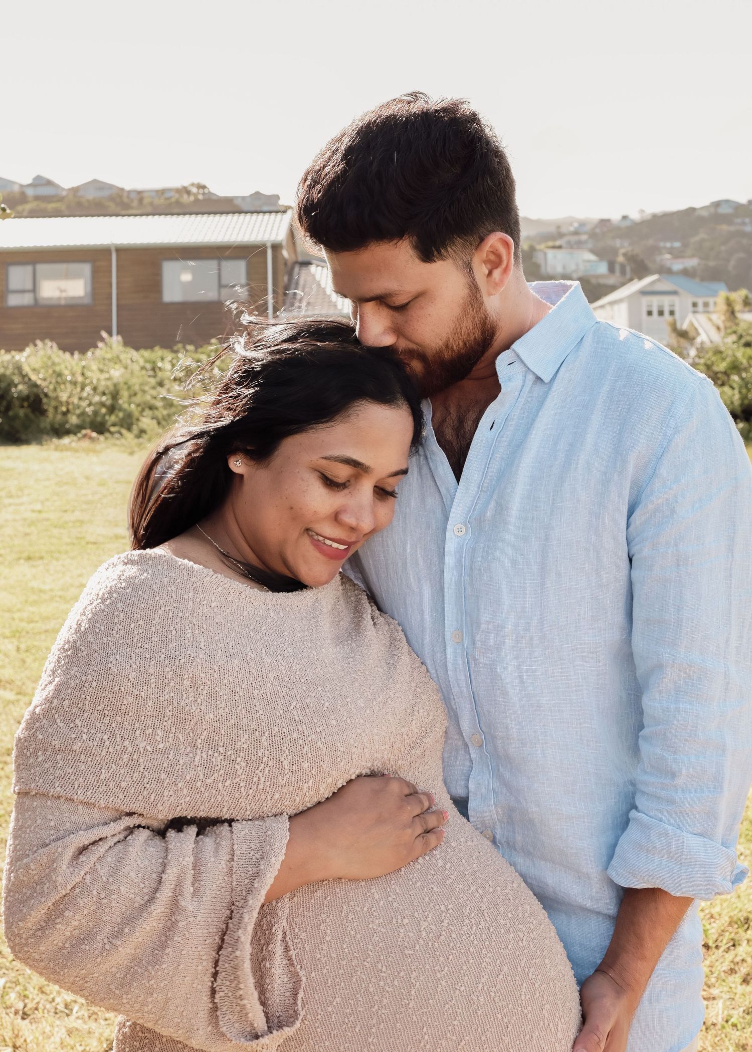 Pregnant couple embracing outdoors at golden hour during a maternity photo shoot session.