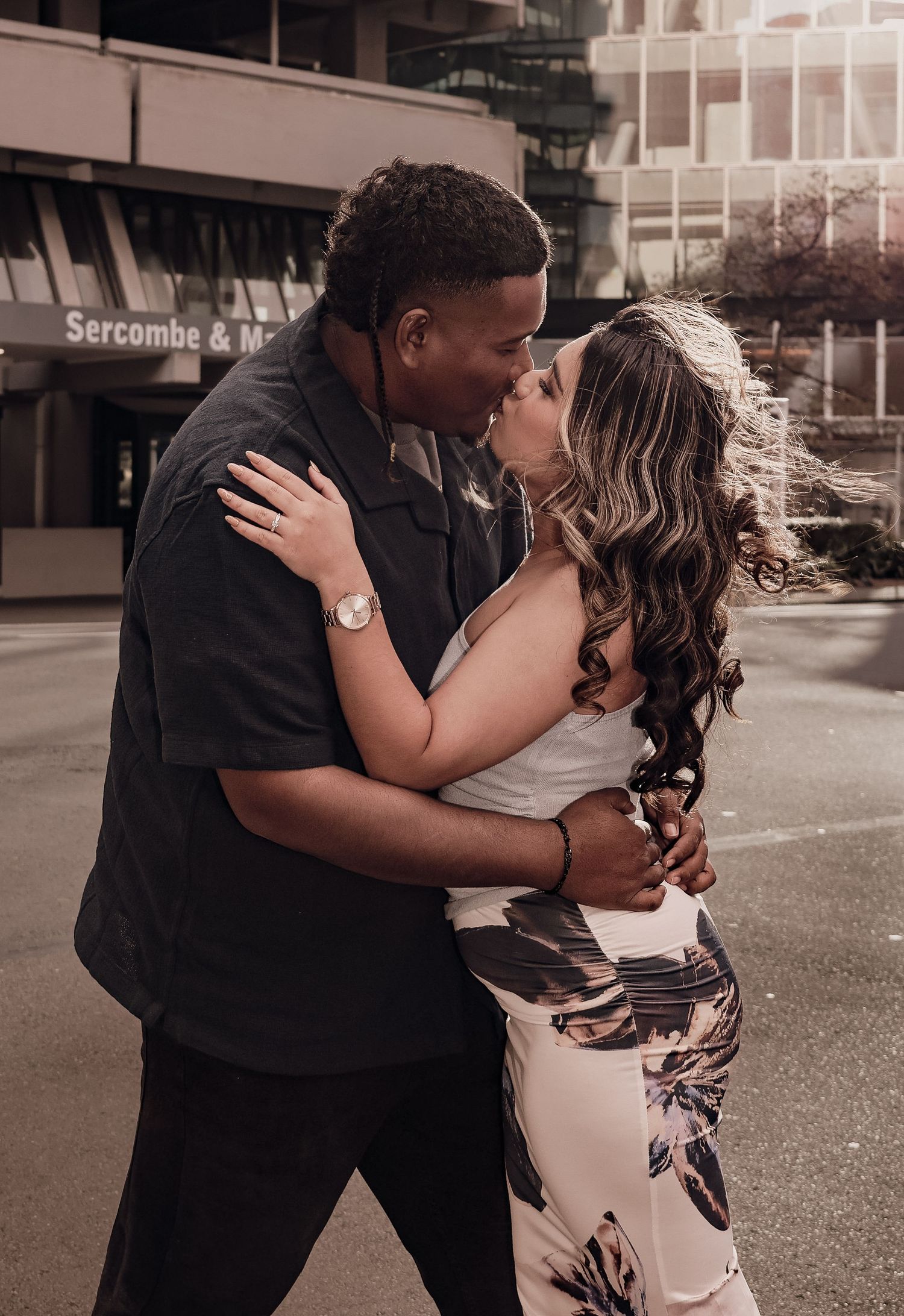 Couple sharing a passionate kiss on a city street, woman in floral skirt and white top.