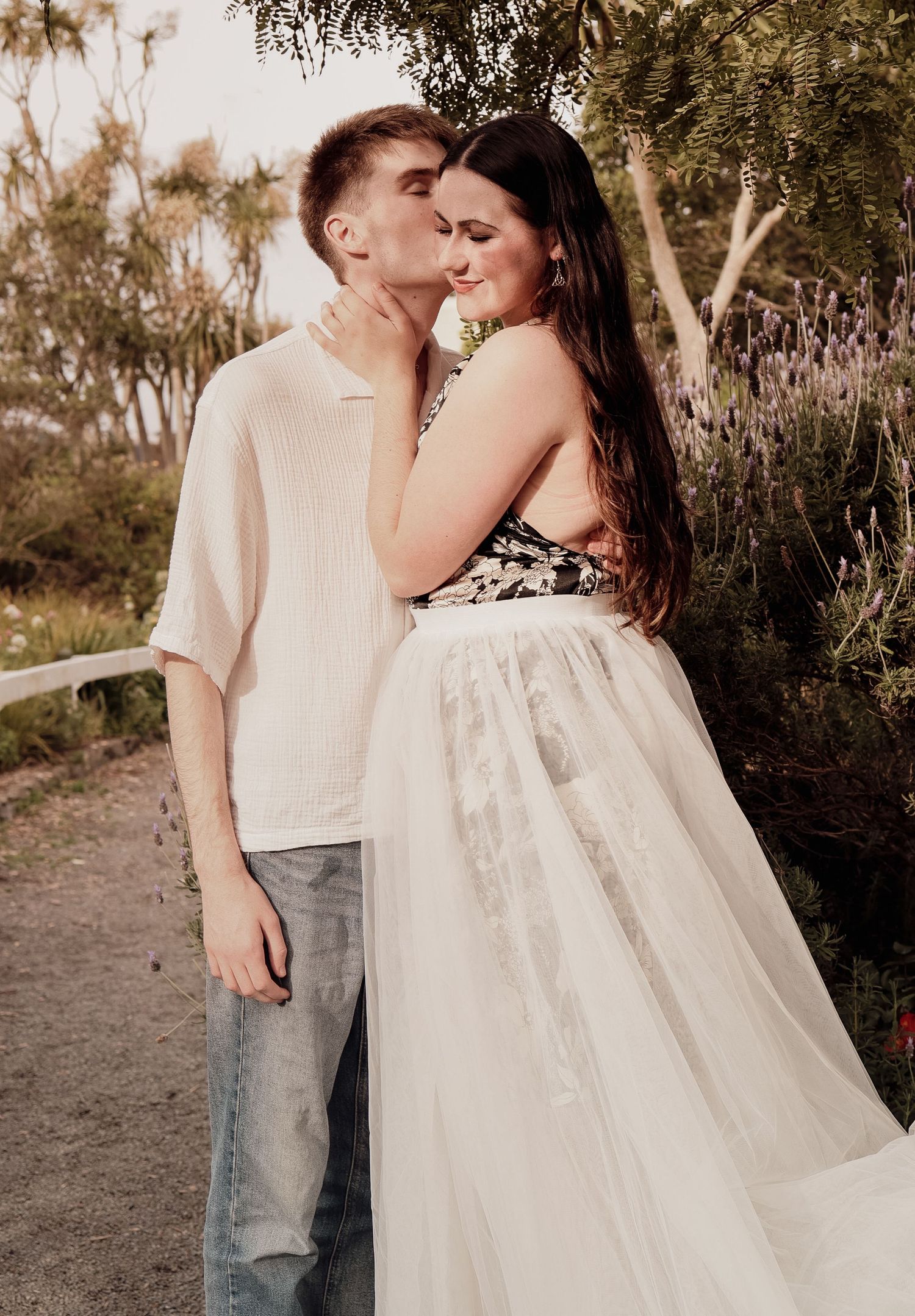 Young couple sharing a tender kiss in a lush garden, woman wearing an elegant white tulle skirt.