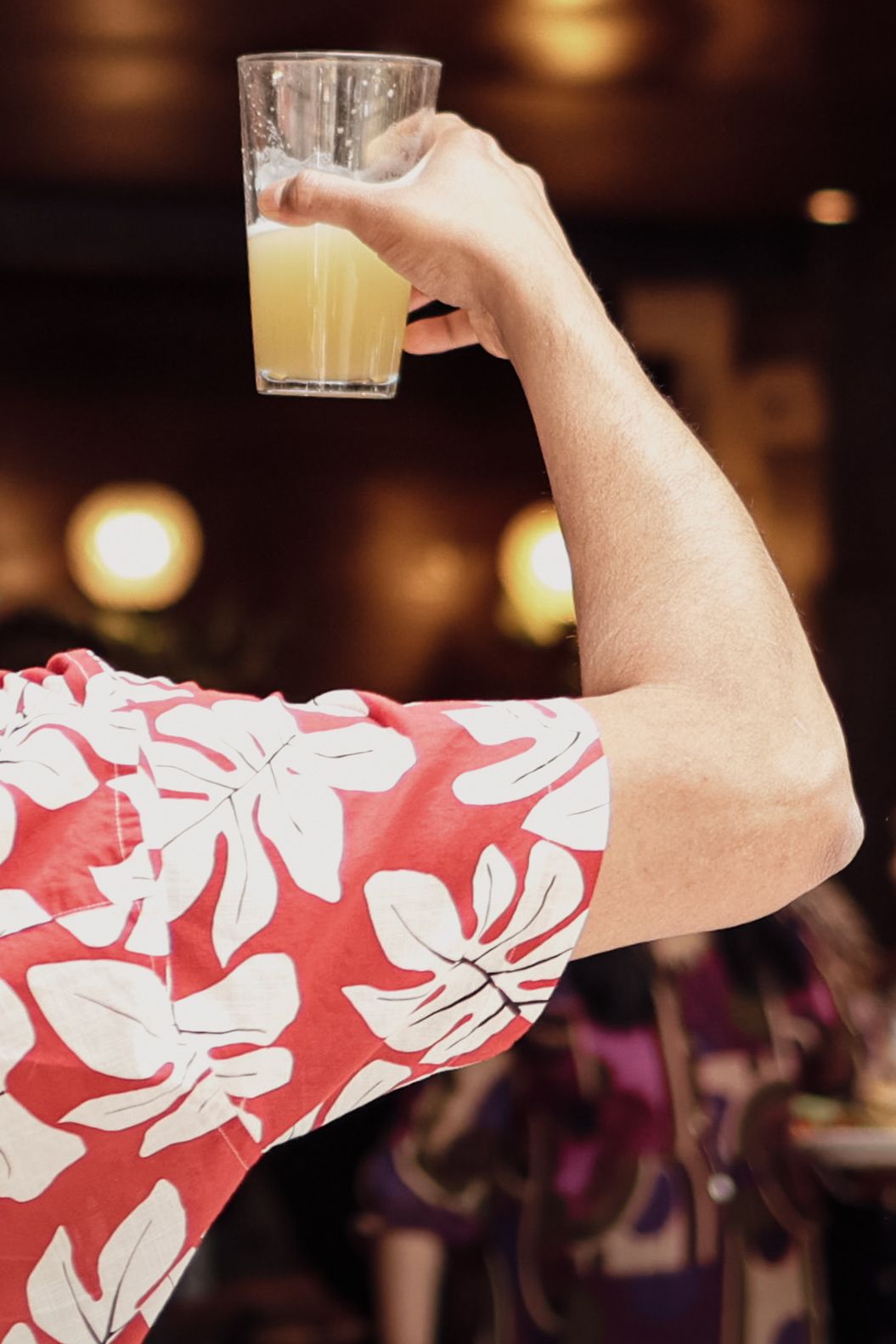 Man in red floral Hawaiian shirt raising a glass of beer at a party celebration.