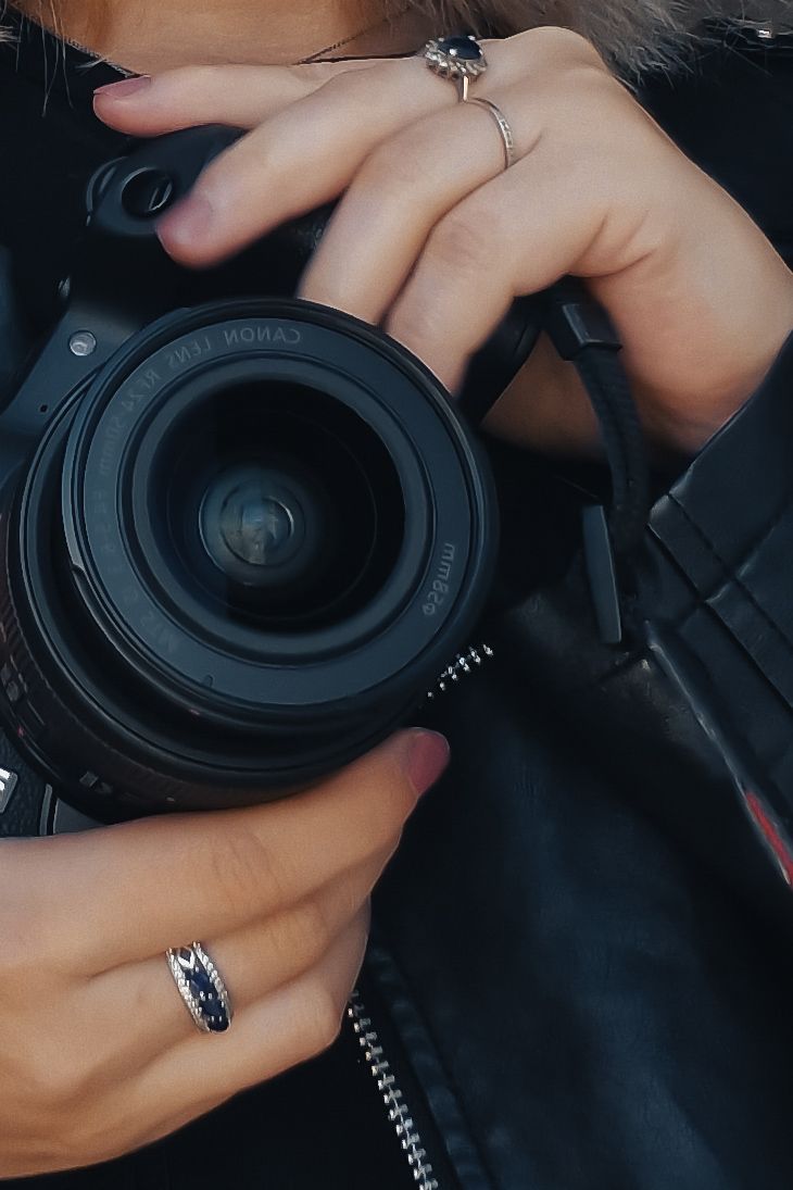 Close-up of a woman holding a black DSLR camera, wearing elegant rings on her fingers.