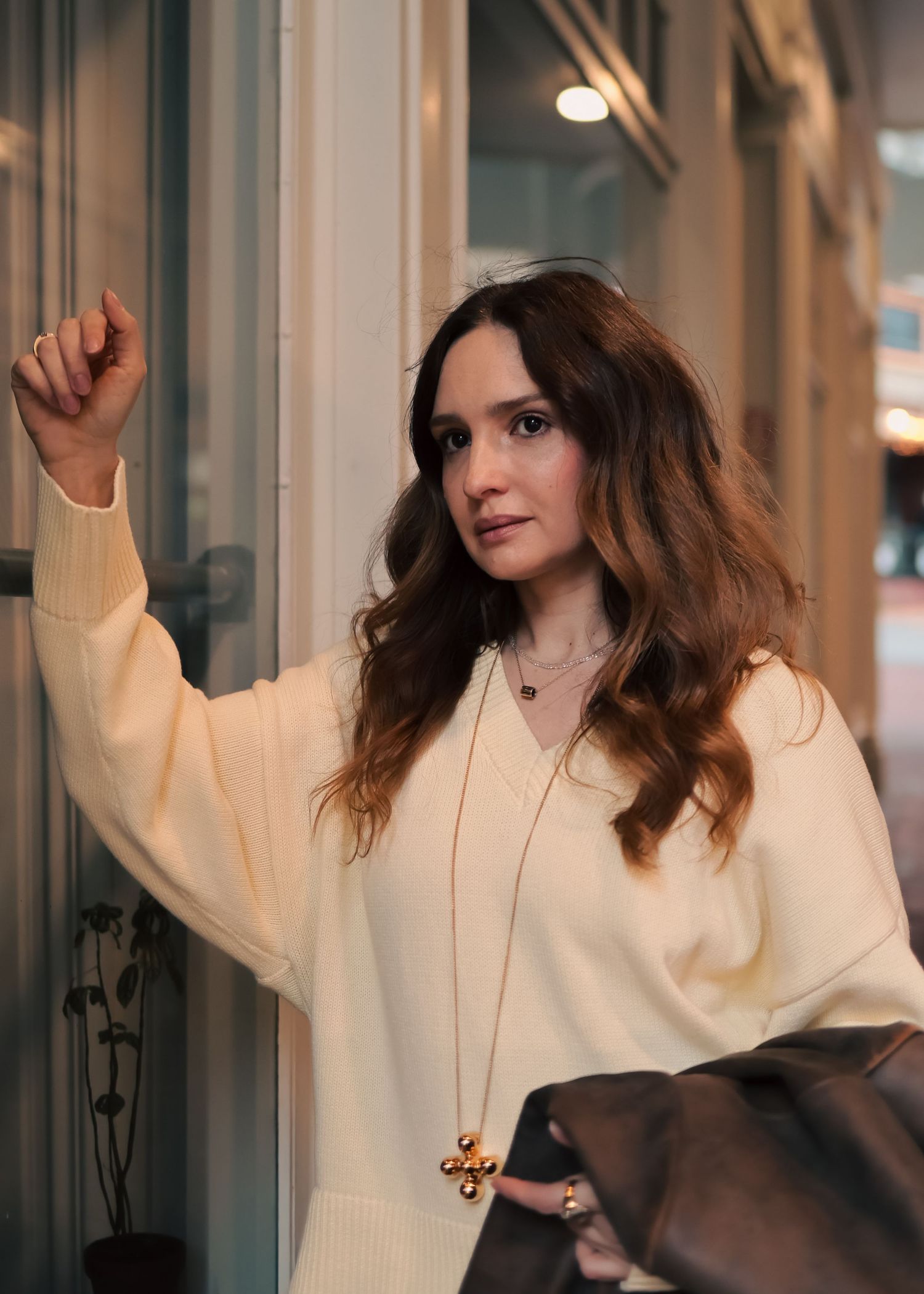Woman in cream sweater with gold necklace reaching for a door handle outdoors.