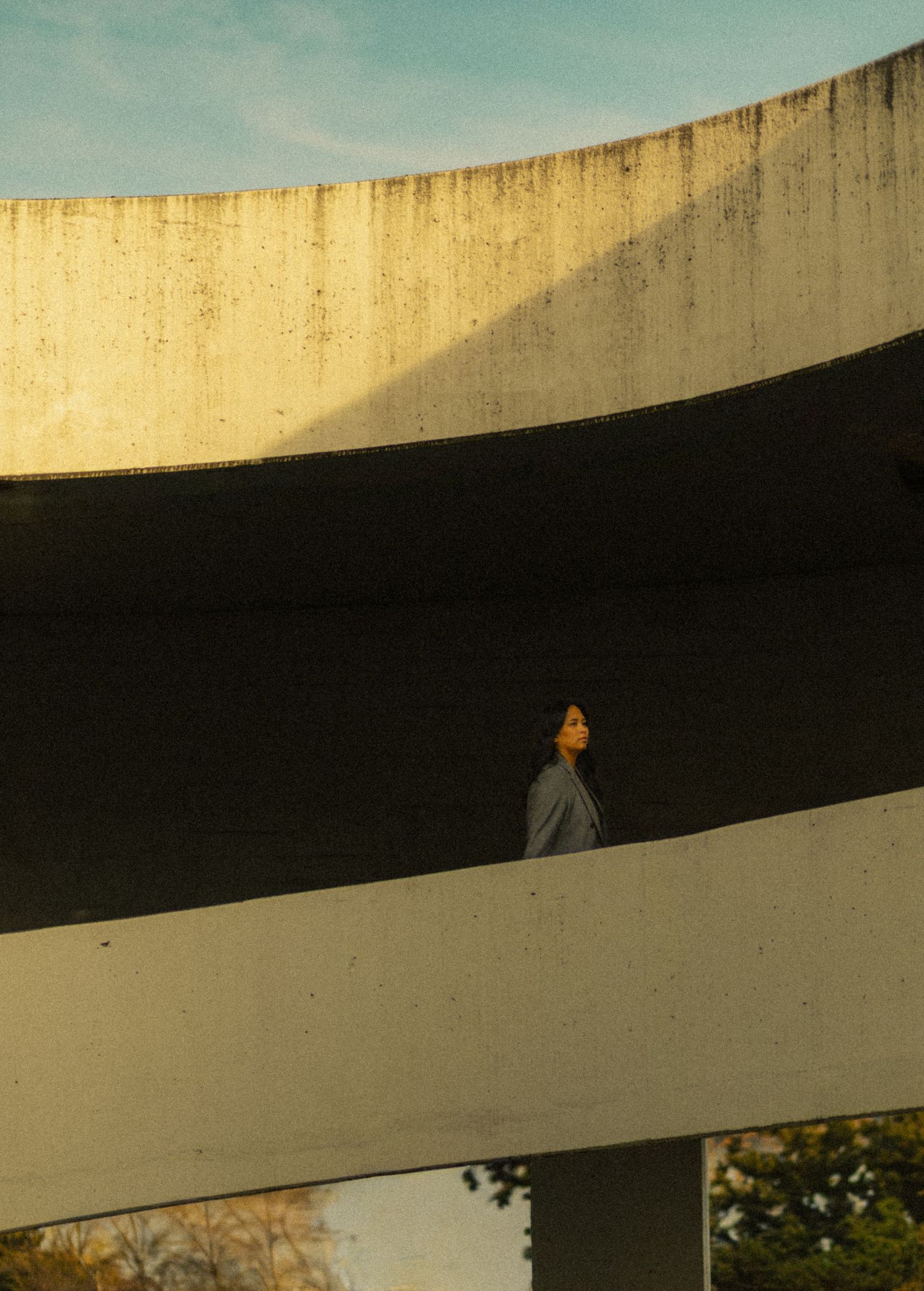 A person stands on a curved concrete structure with bold stripes, bathed in golden light against a blue sky.