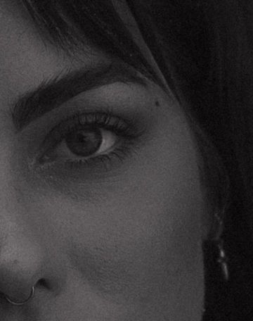 Close-up black and white portrait of a young woman with bold brows, nose ring, and hoop earring.