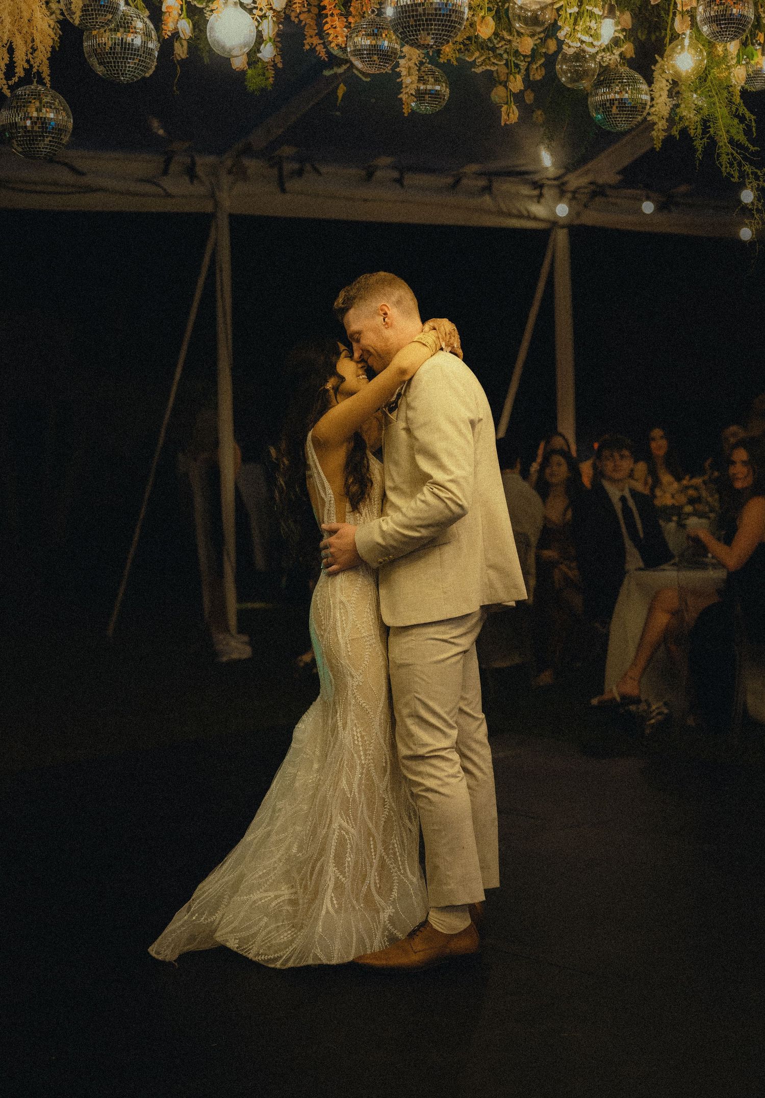 Bride and groom share their first dance under disco balls and floral decor at a romantic wedding reception.