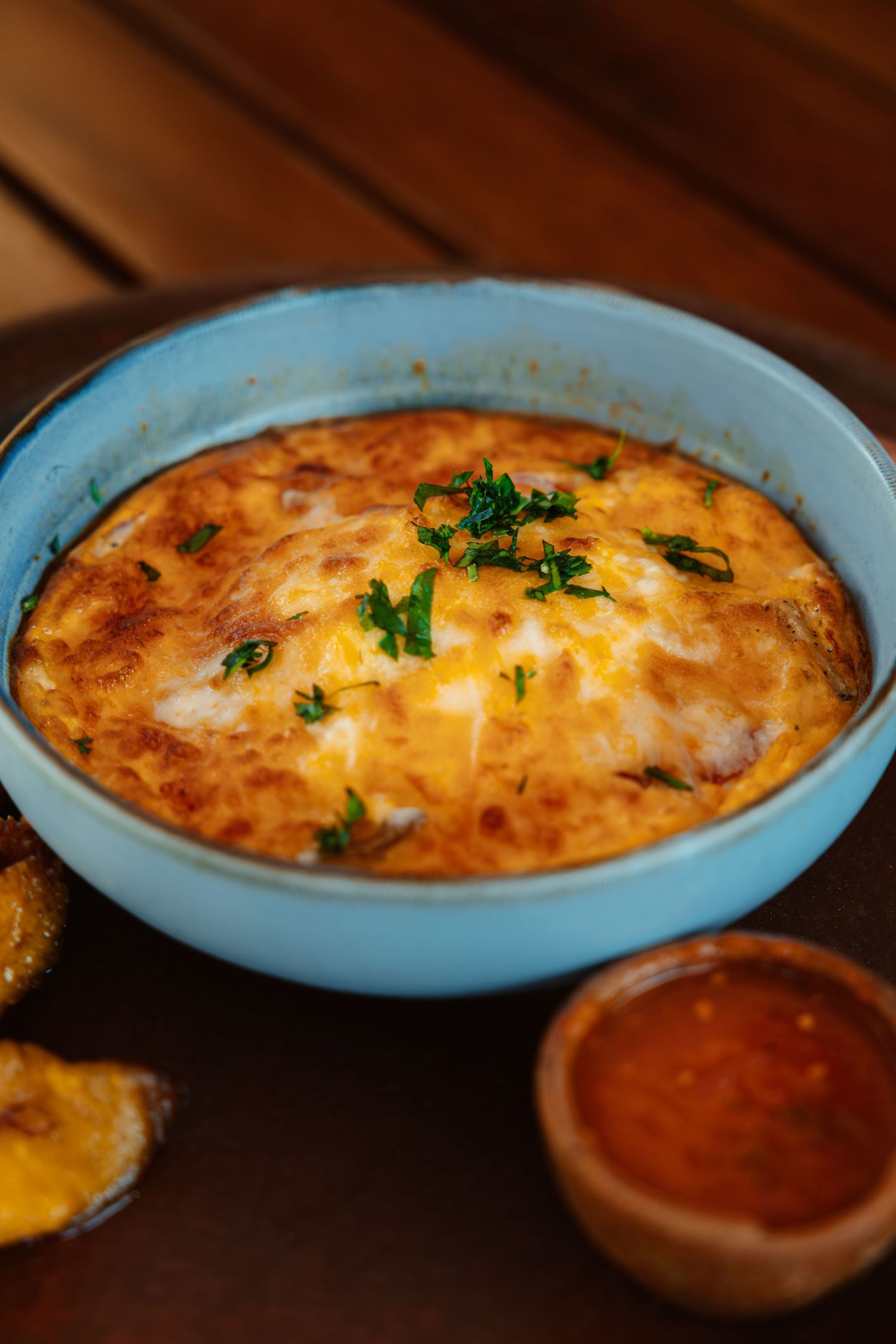 Golden baked egg casserole in a blue ceramic dish garnished with fresh parsley, served with dipping sauce.