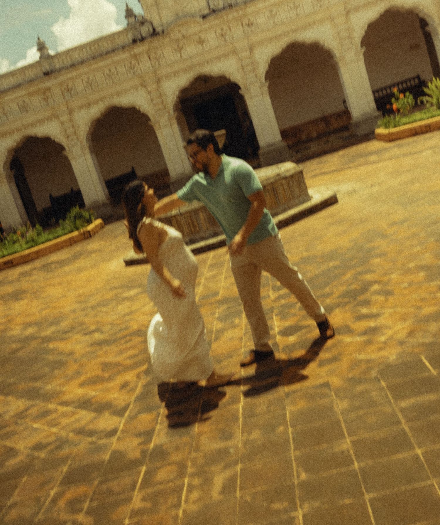 Couple dancing together in a sunlit courtyard of a historic white colonial building with arched architecture.
