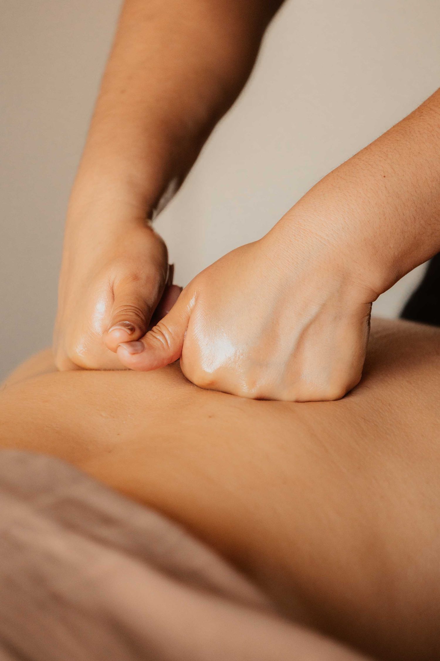 Massage therapist using knuckles to perform deep tissue back massage on client at spa.