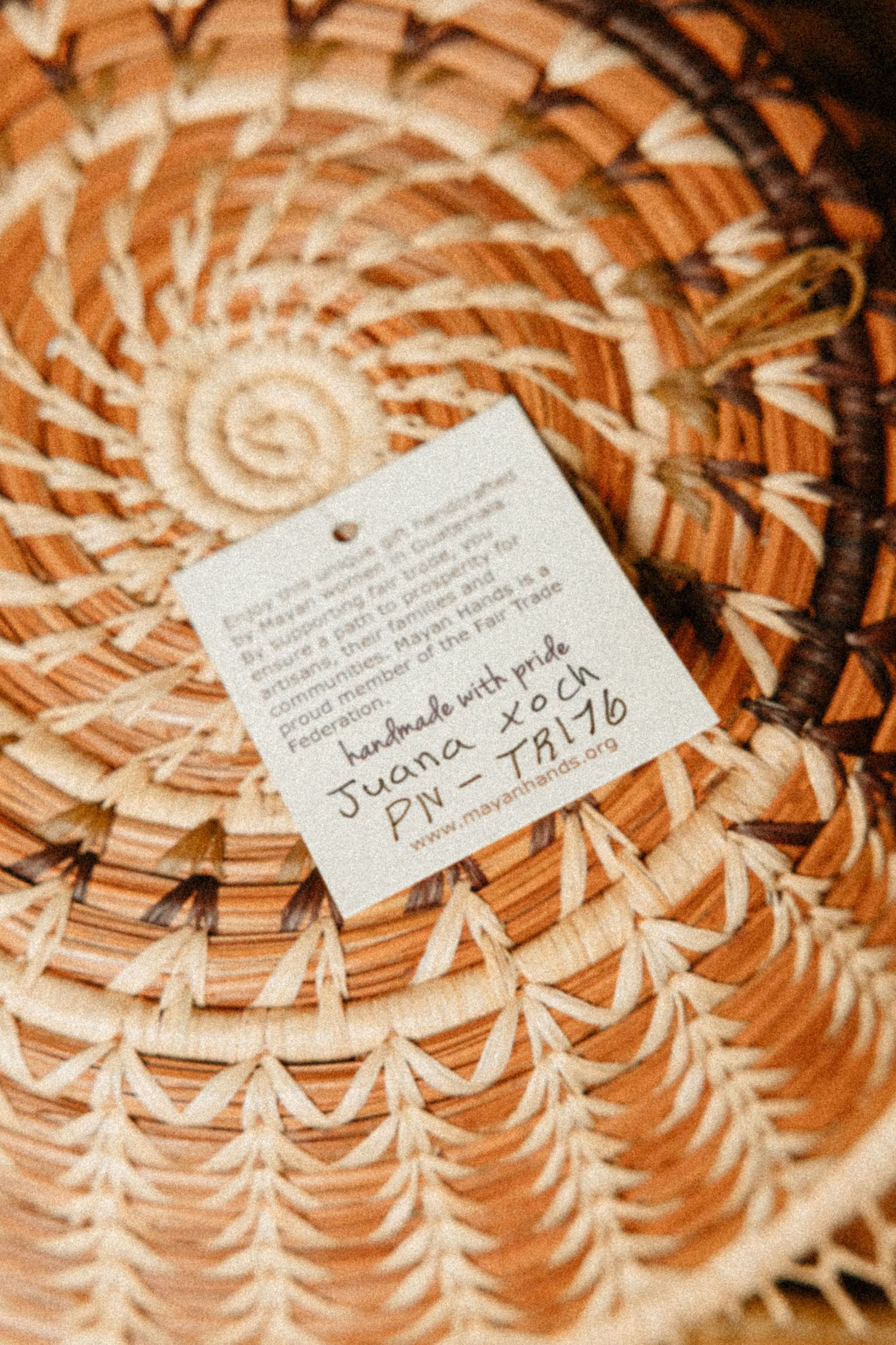 Handwoven Fair Trade basket with artisan tag signed by Juana, showcasing intricate spiral pine needle weaving pattern.