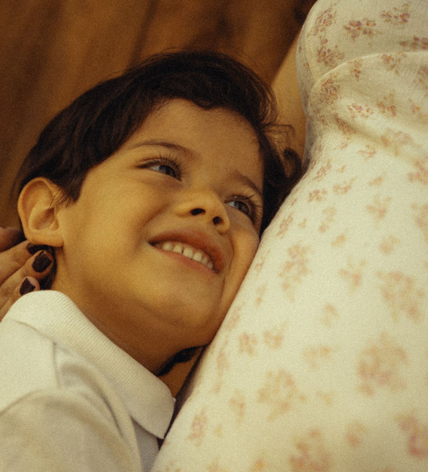 A smiling young child resting against a floral fabric, looking up with a joyful expression.