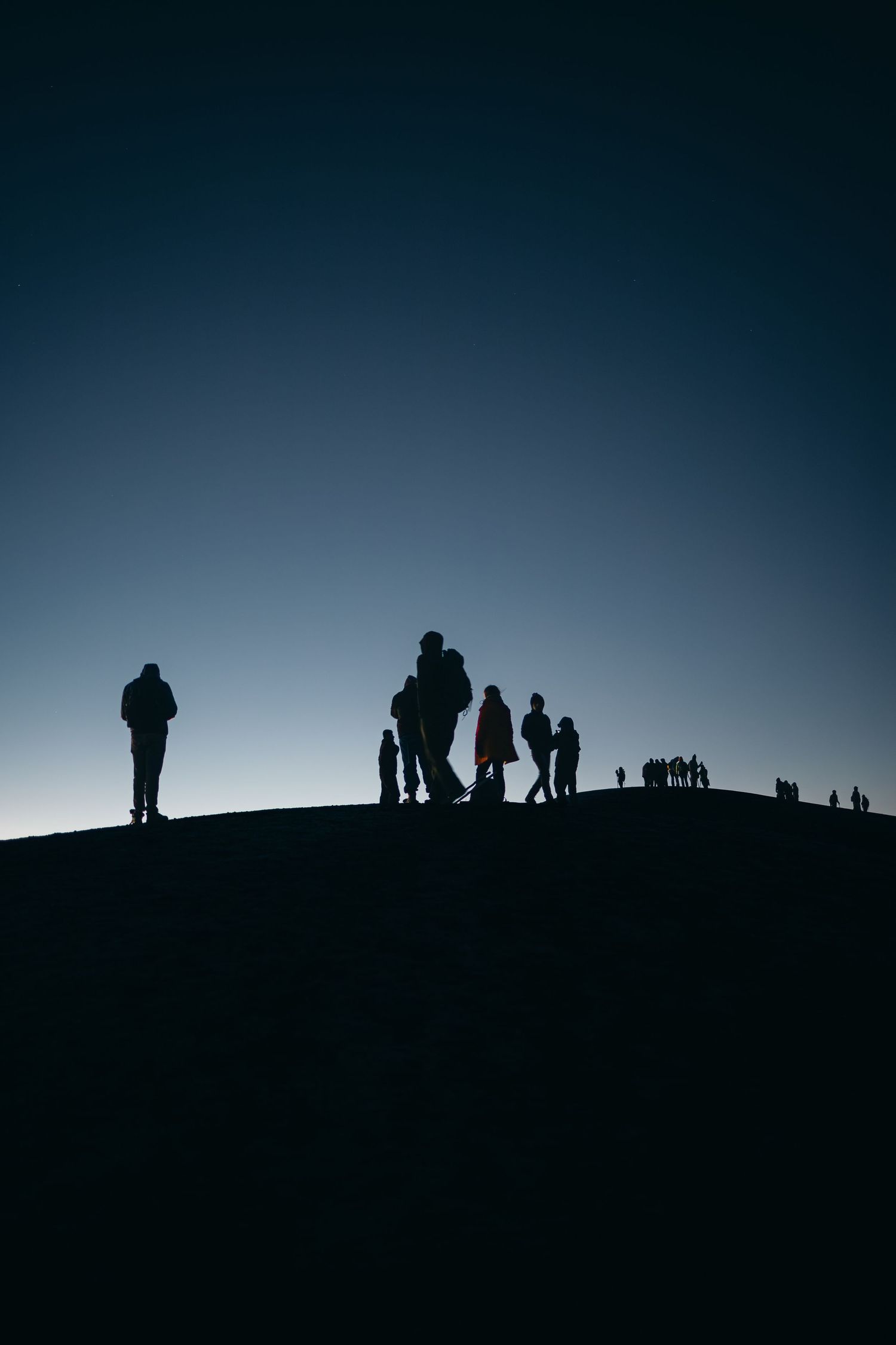 Silhouettes of people standing on hilltop ridge against deep blue twilight sky.