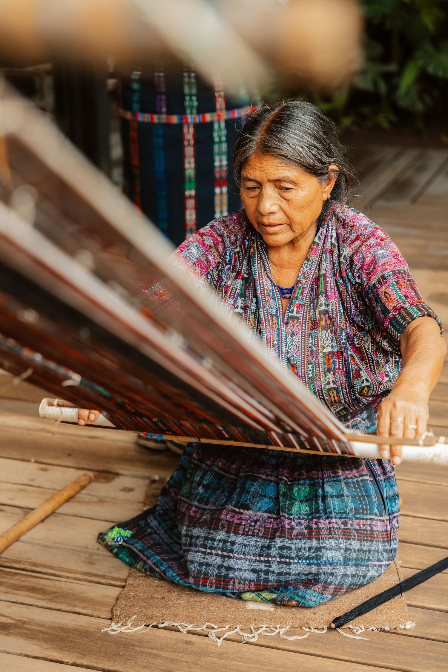Indigenous Guatemalan woman in traditional huipil concentrating while working on a backstrap loom outdoors.