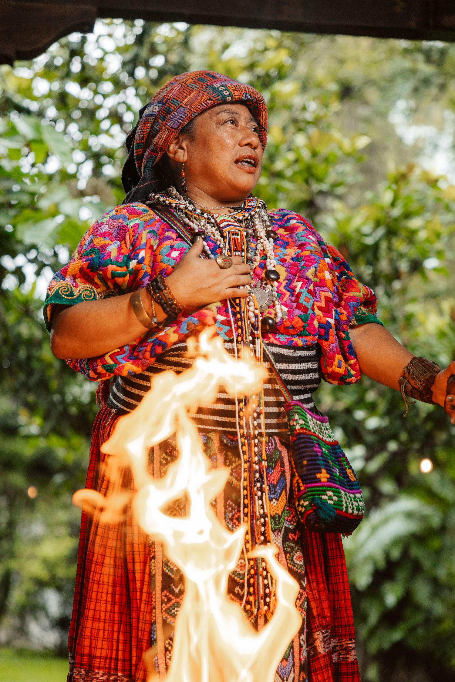 Indigenous woman in traditional colorful Guatemalan attire performing a fire ceremony outdoors.