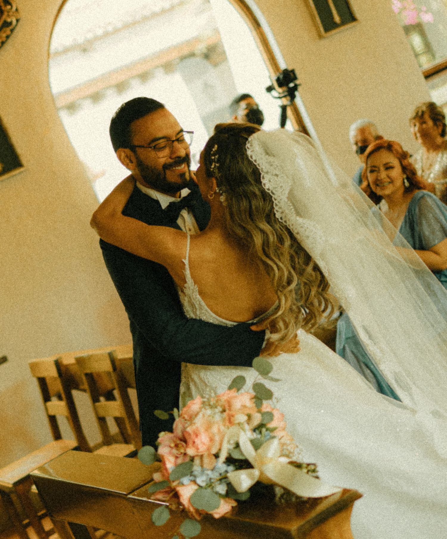 A bride and groom share a joyful embrace at the altar during their wedding ceremony, with guests smiling in the background.