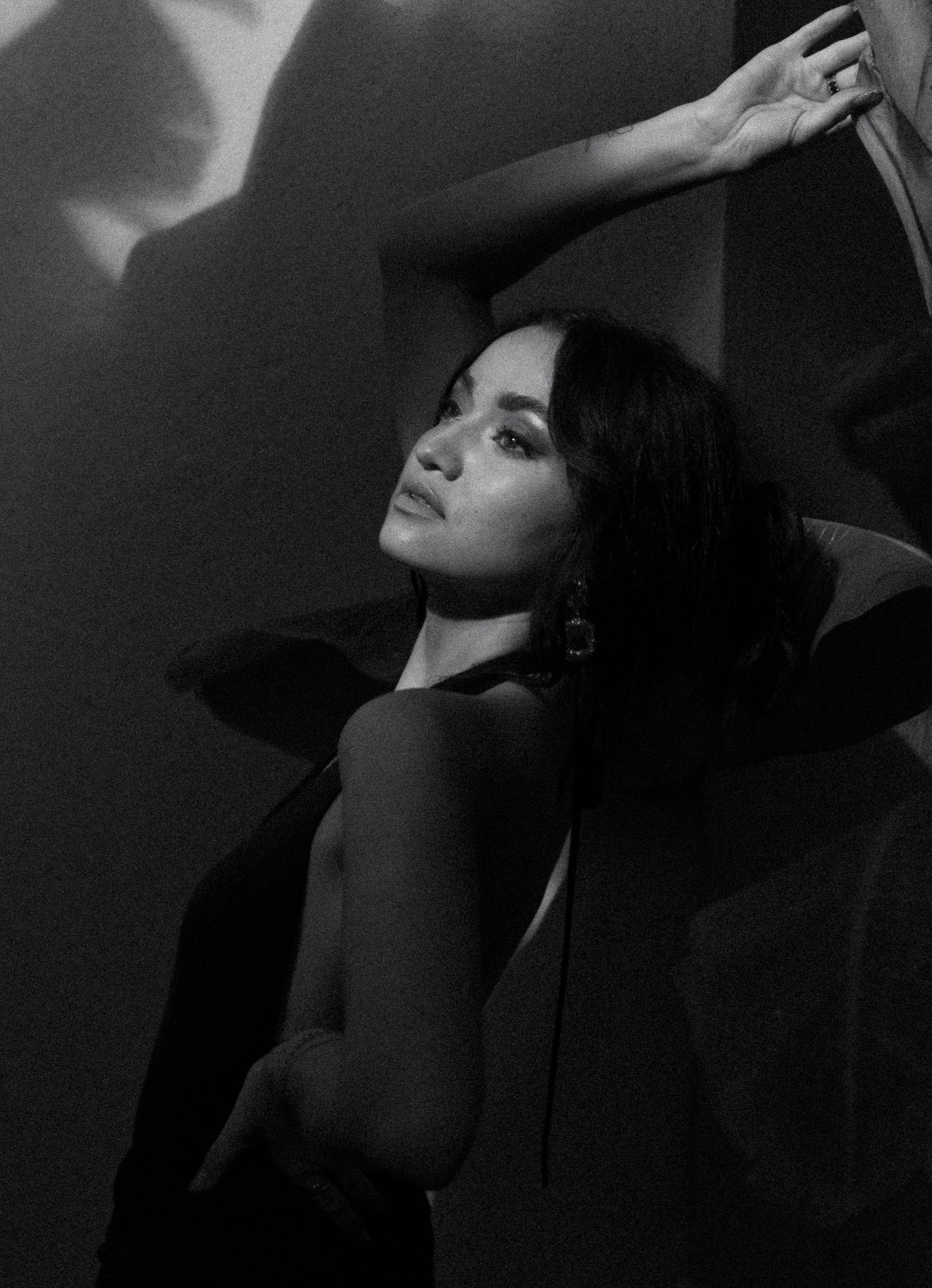 Black and white portrait of a woman with dark hair posing dramatically against a wall with artistic shadows.