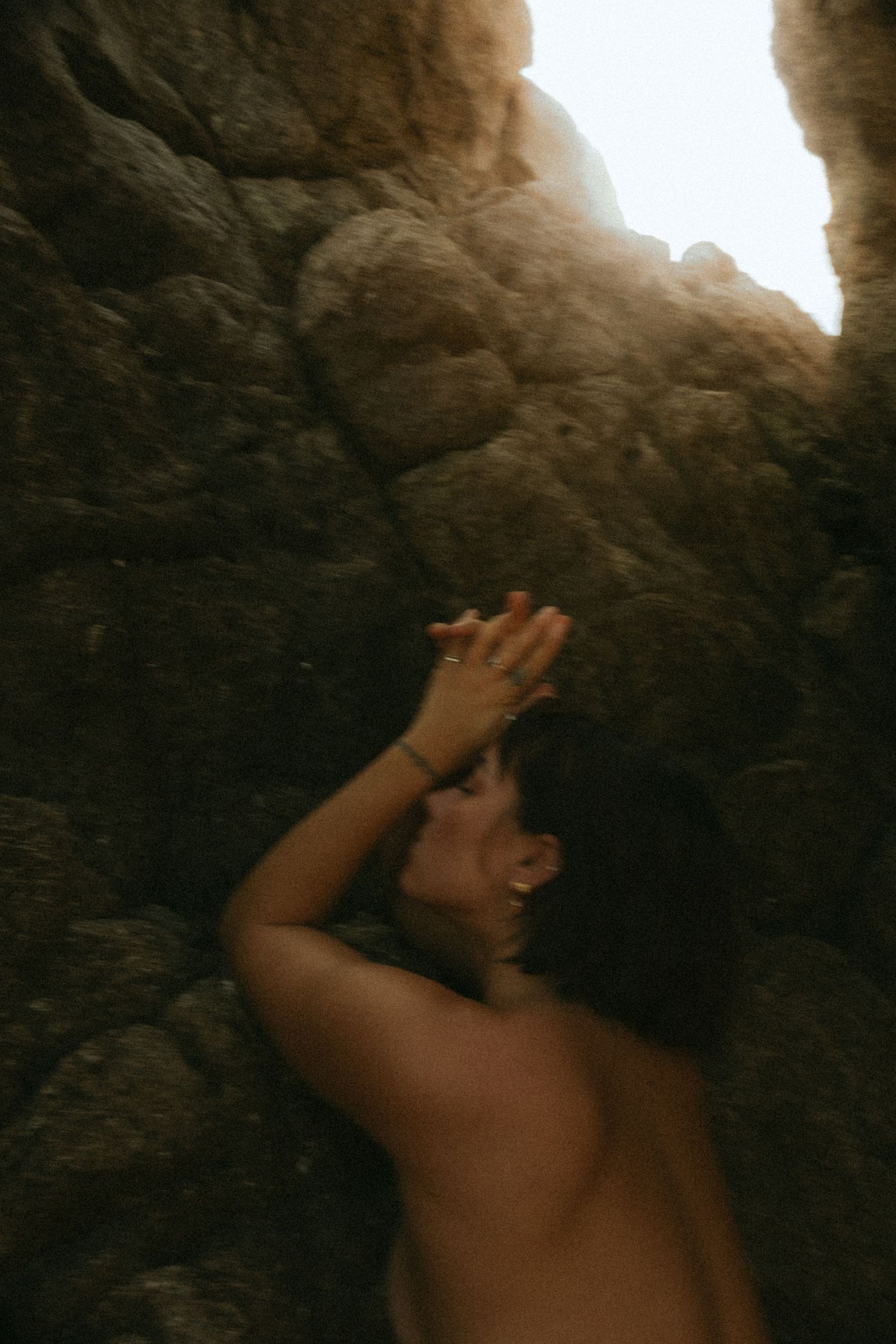 Person leaning against sunlit rock cave wall with hand raised to forehead.