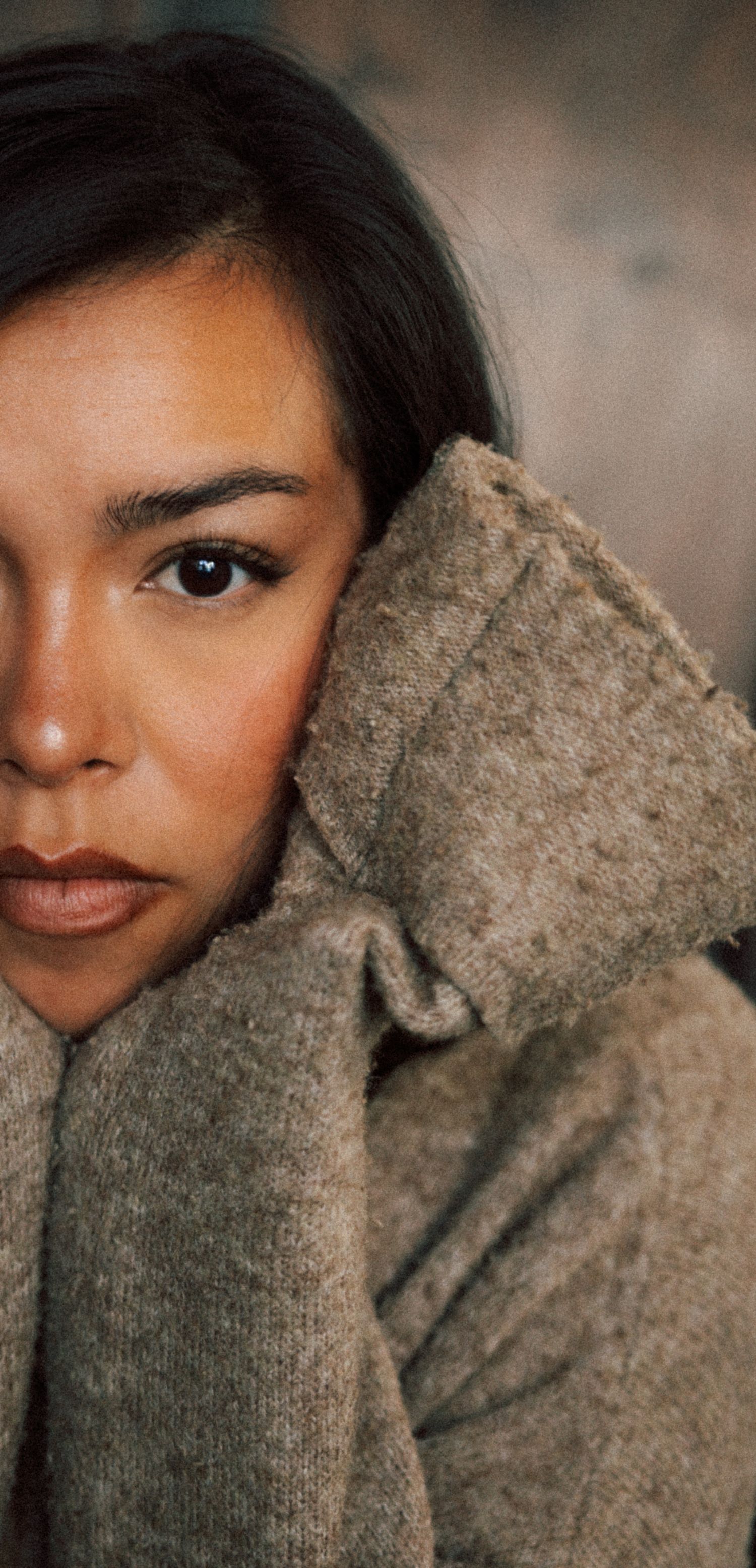 Close-up portrait of a woman in a gray wool sweater with a thoughtful expression in soft light.