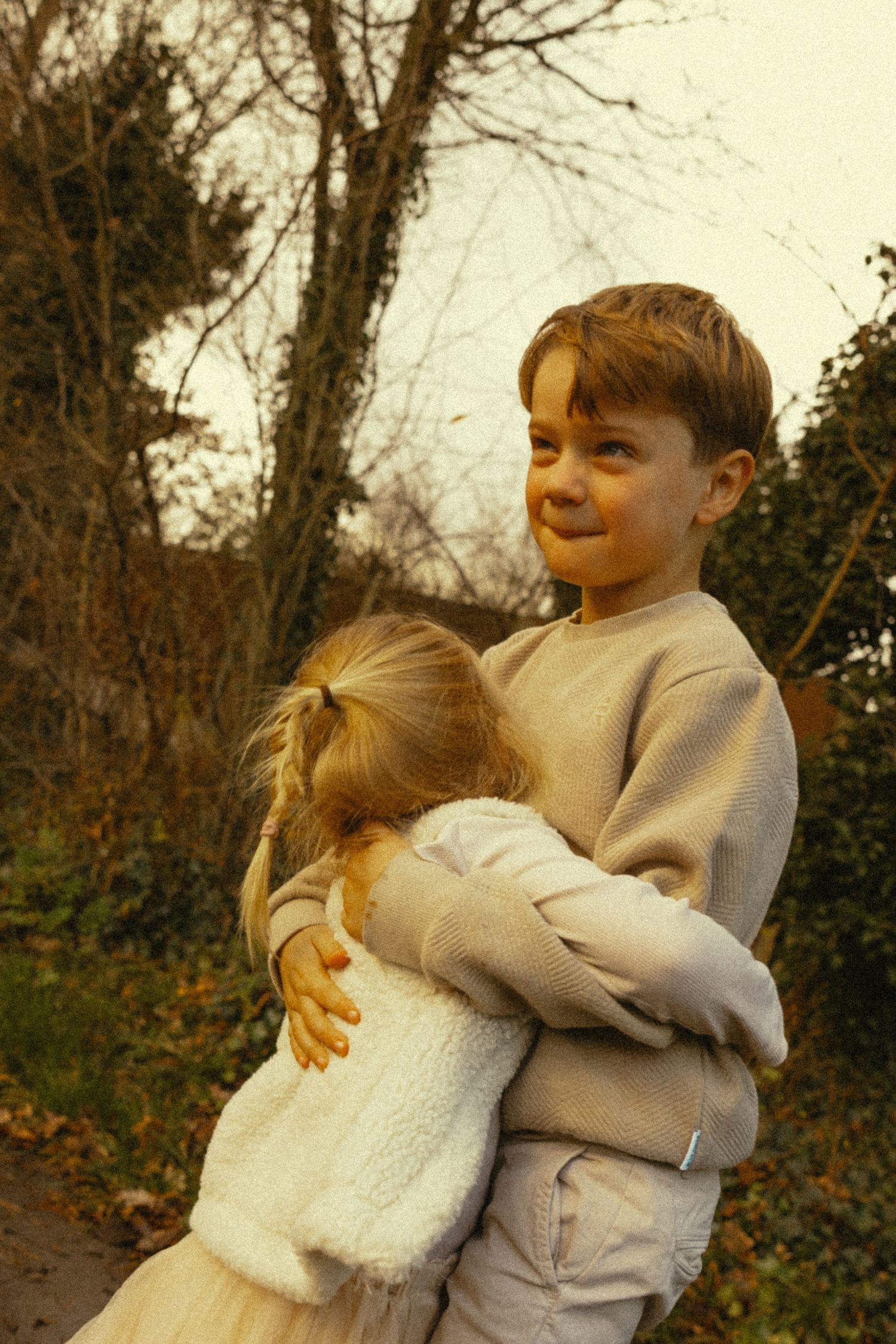 Young boy smiling while hugging little blonde girl outdoors in autumn.