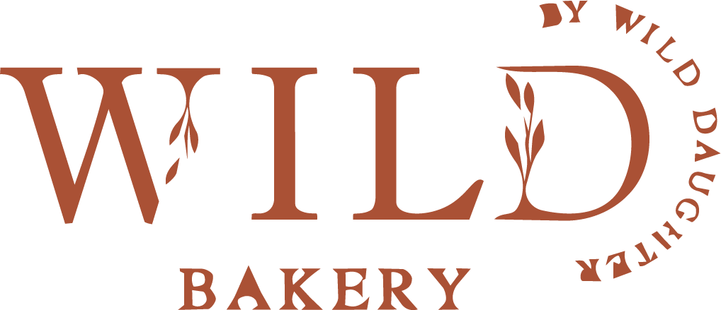 Wild Bakery by Wild Daughter rustic terracotta logo featuring bold typography with delicate botanical leaf illustrations.