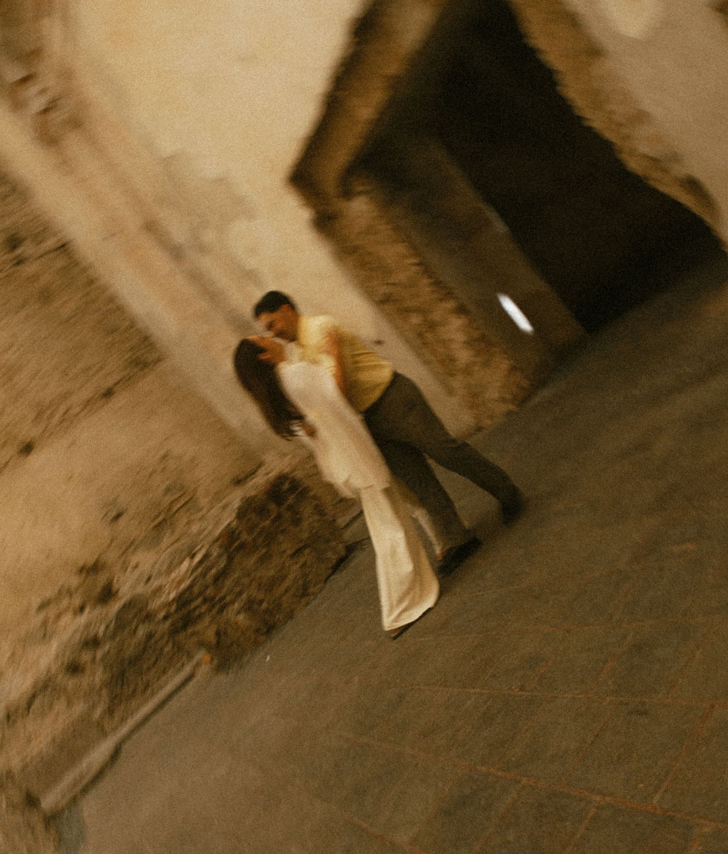 Couple sharing a romantic kiss in a rustic stone archway, captured at a tilted angle.
