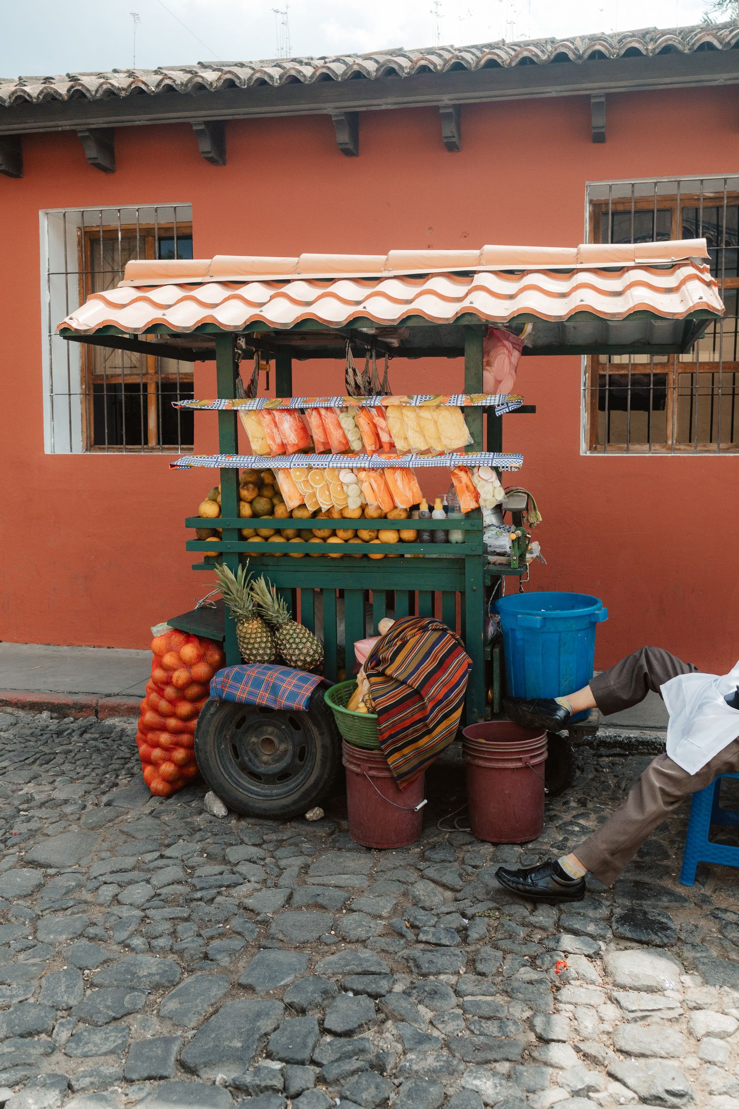 Colorful street fruit cart with pineapple and produce on cobblestone street in front of a red building.