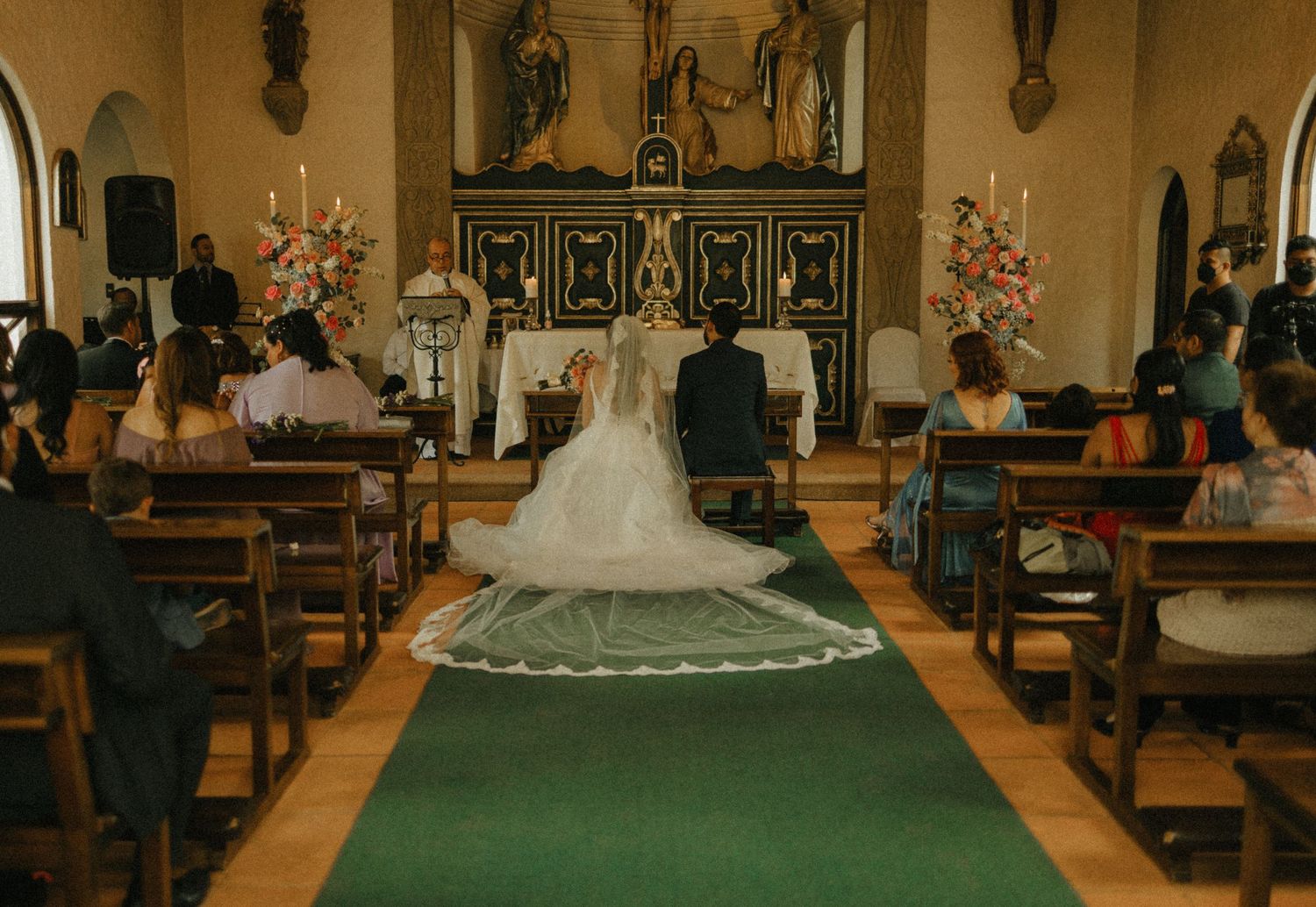 Bride and groom kneeling at church altar during wedding ceremony with guests seated in wooden pews.