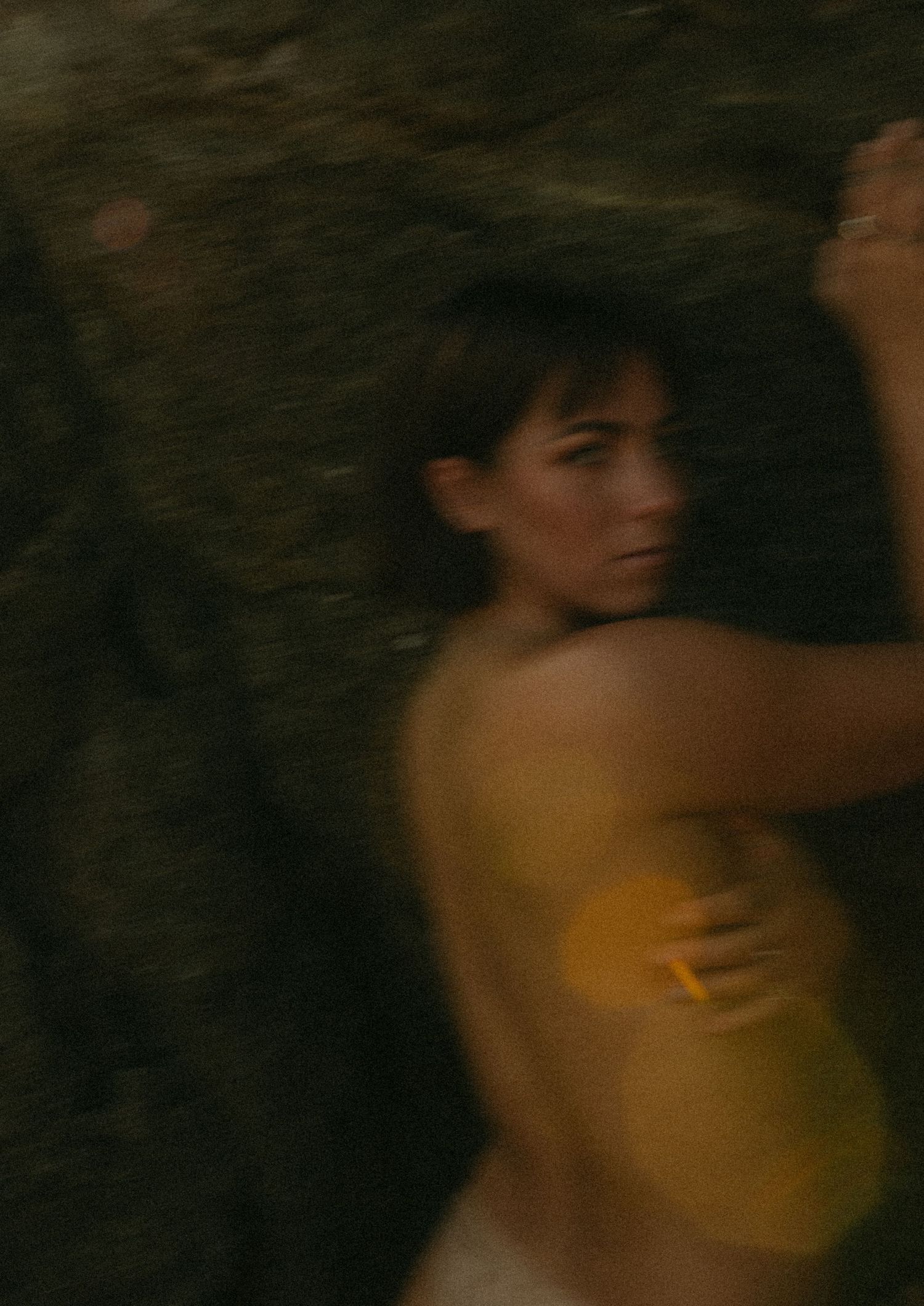 A woman in a yellow top lies against a dark rocky surface, gazing softly to the side.